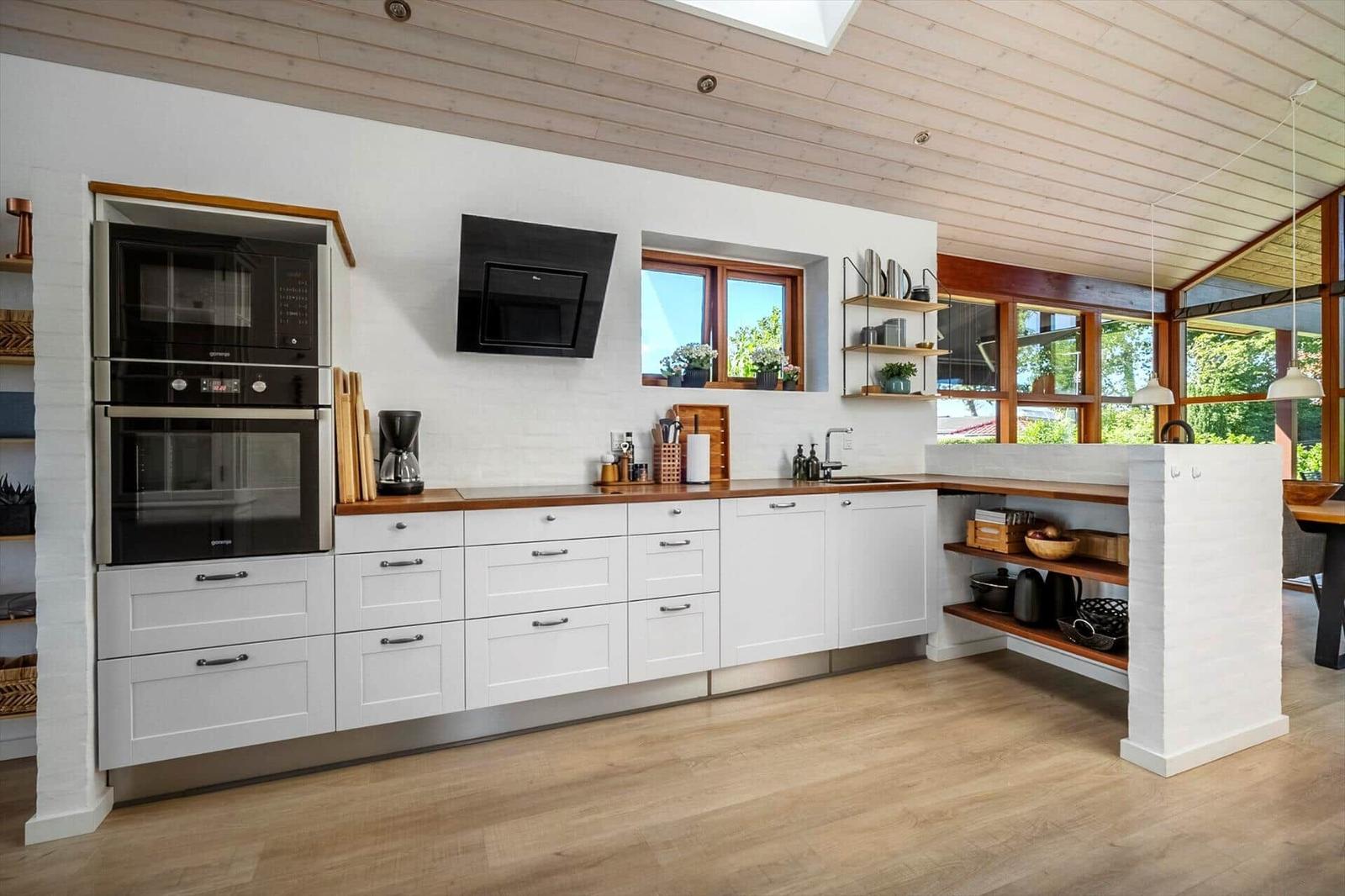 Moderne Küche mit weißen Schränken, Holzoberflächen und integriertem Backofen.