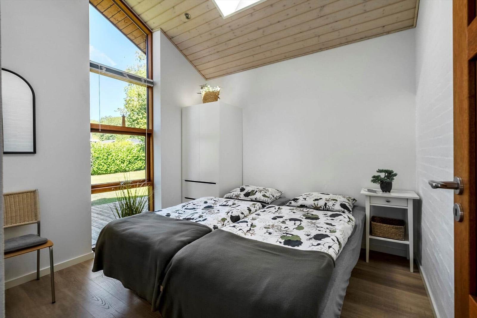 Schlafzimmer mit Doppelbett, großem Fenster und Holzdecke.