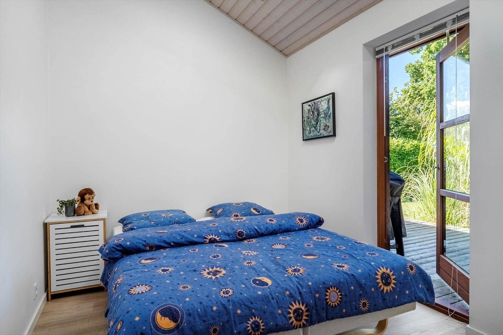 Schlafzimmer mit Bett, Nachttisch und Fenster zur Terrasse.