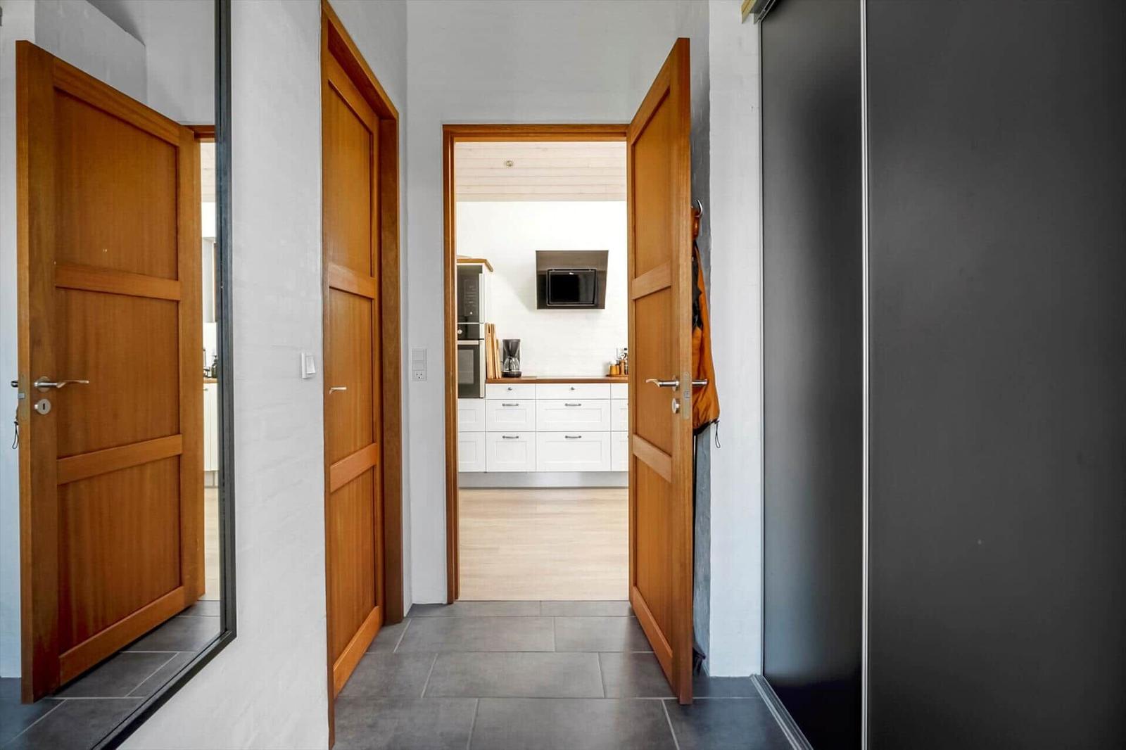 Hausgang mit Holztüren und Blick in die Küche mit weißen Schränken.