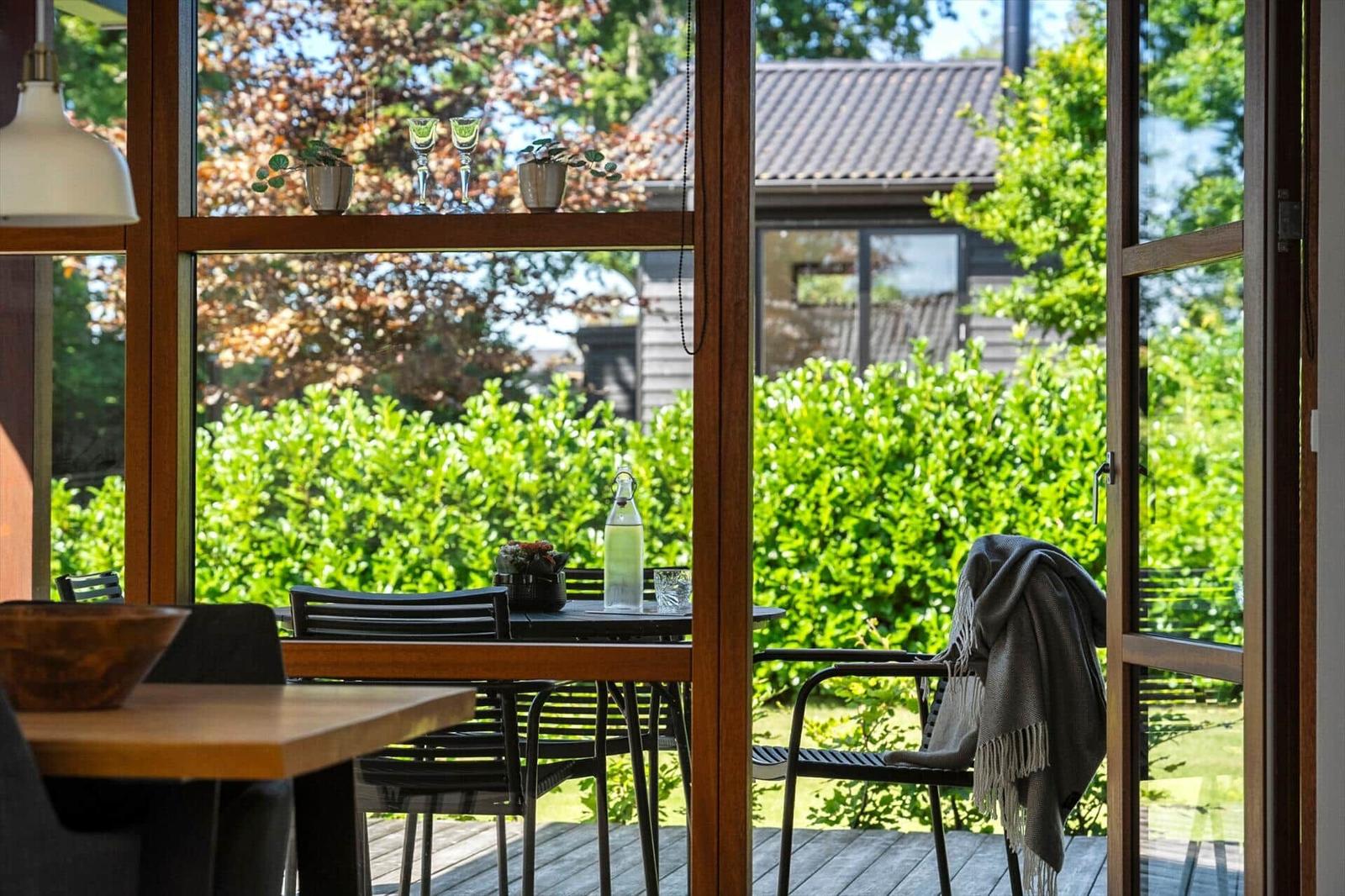Terrasse mit Tisch, Stühlen und Decke. Blick auf grüne Hecke und Haus.