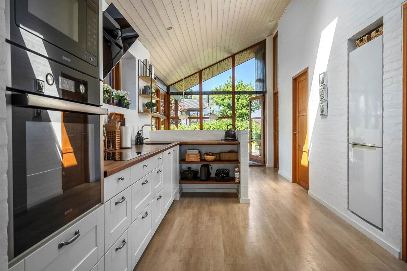 Moderne Küche mit Holzboden, weißen Schränken und großem Fensterblick.