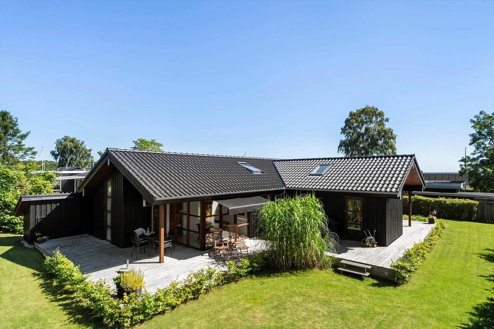 Moderne Holzhütte mit Terrasse und Garten unter blauem Himmel.