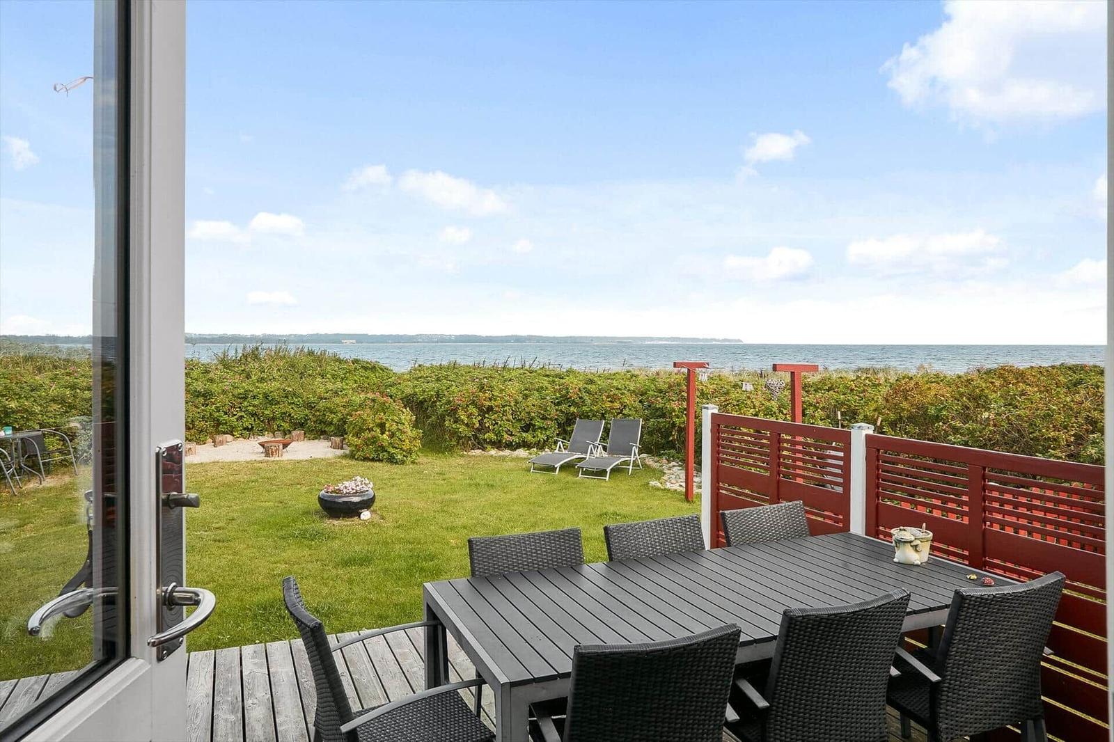 Terrasse mit Tisch und Stühlen, Blick auf Grünflächen und Meer.