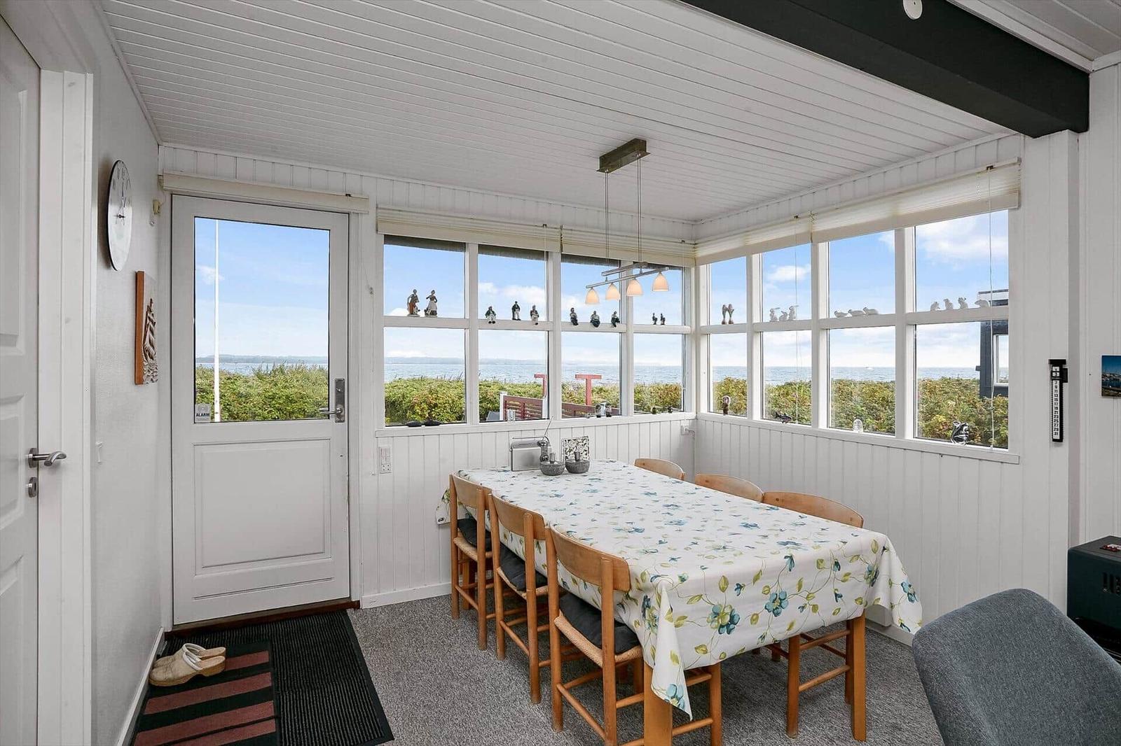 Esszimmer mit Tisch, Stühlen und Meerblick durch große Fenster.