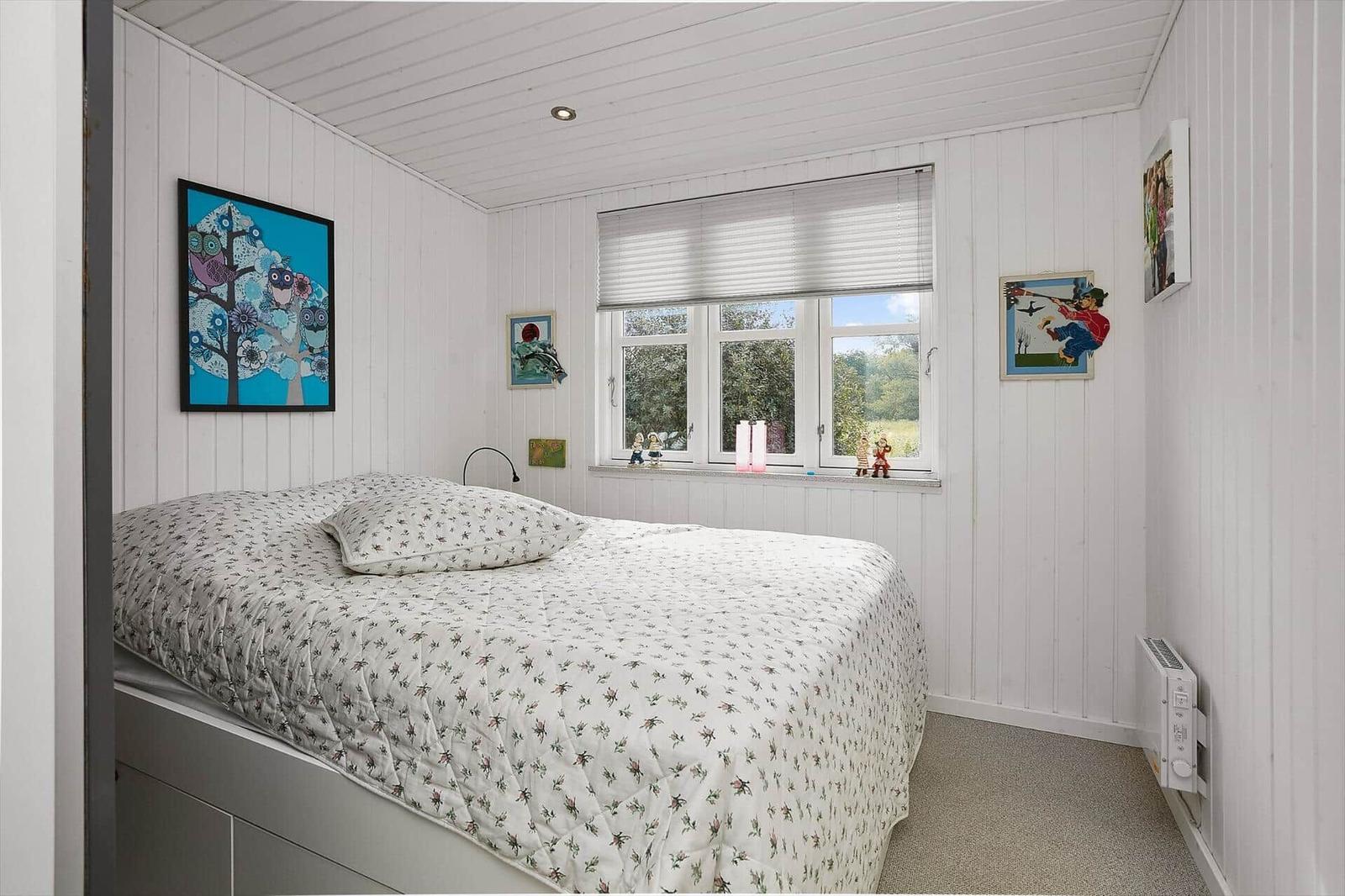 Schlafzimmer mit Bett, Fenster und Wandbildern.