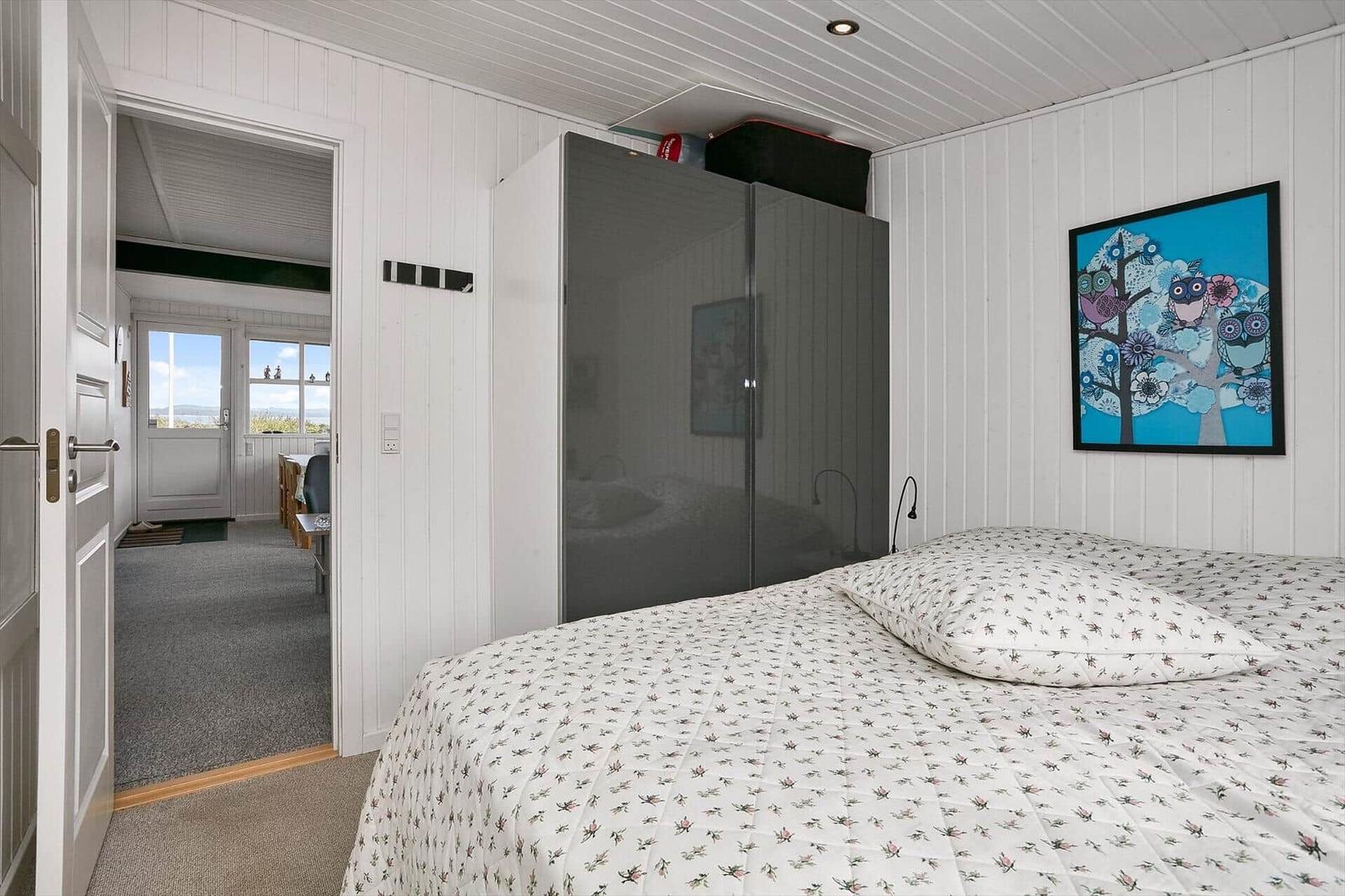 Schlafzimmer mit Bett, Kleiderschrank und Wandbild. Durchgang zur Küche und Terrasse.