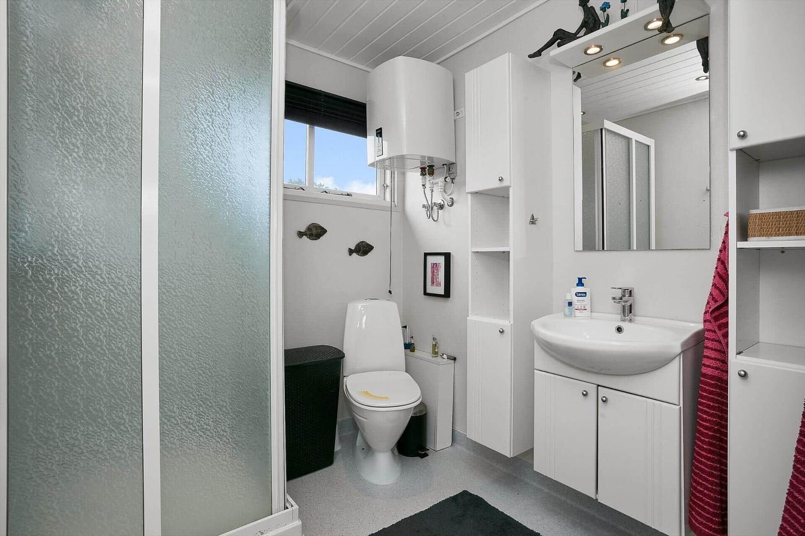 Badezimmer mit Toilette, Waschbecken und Dusche. Weiße Einrichtung und Fenster mit Blick.