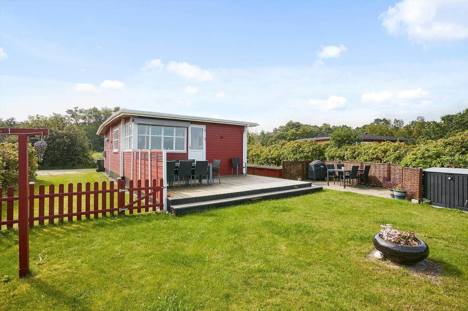 Rotes Ferienhaus mit Terrasse und Garten. Grill und Sitzgelegenheiten vorhanden.