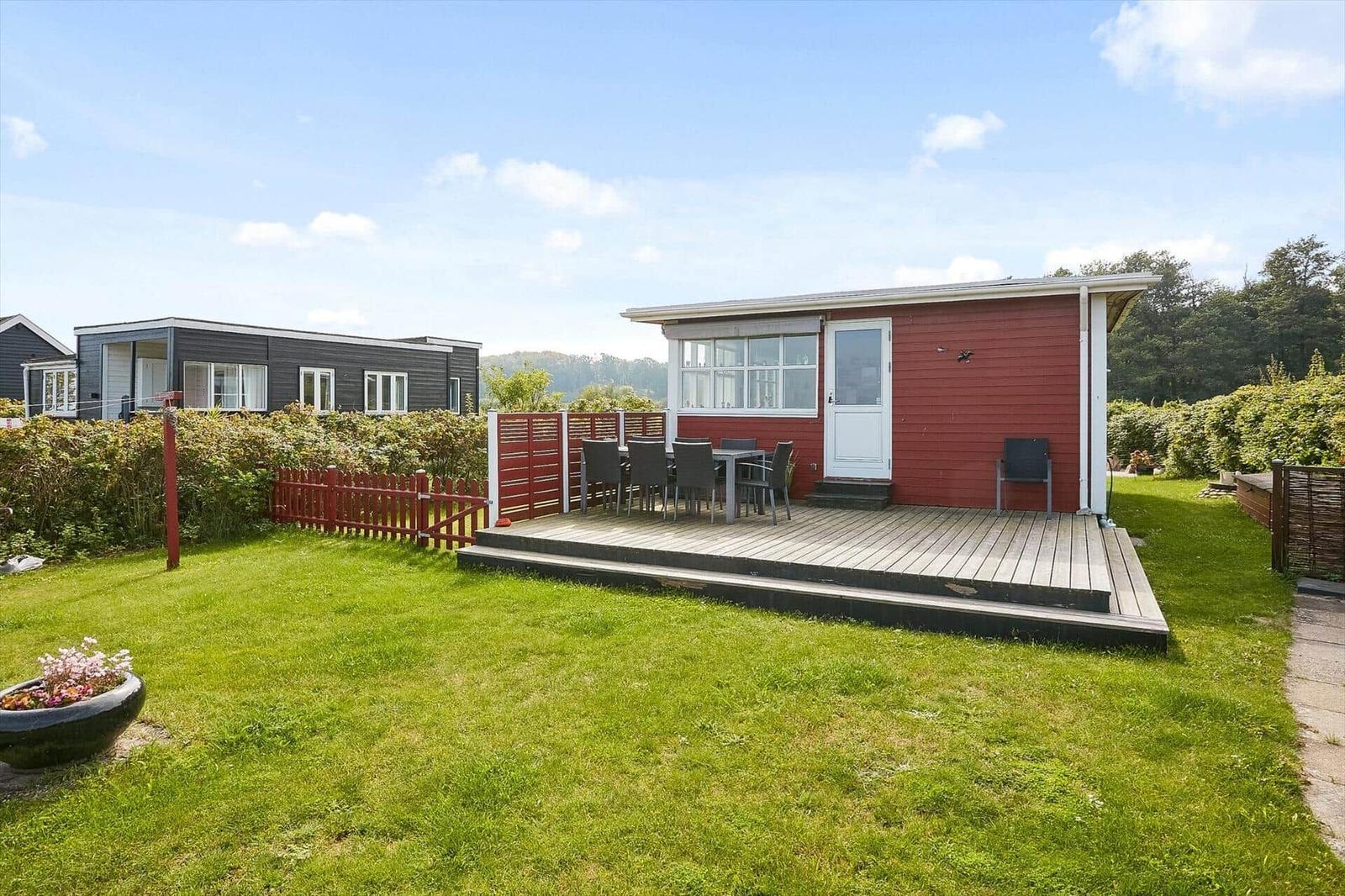Rotes Ferienhaus mit Terrasse und Garten. Tisch und Stühle auf der Veranda.