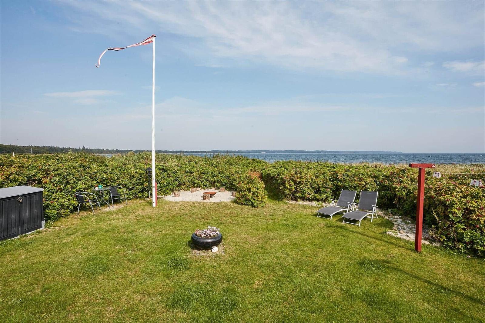 Grüner Garten mit Liegestühlen, Feuerplatz und Blick aufs Meer.