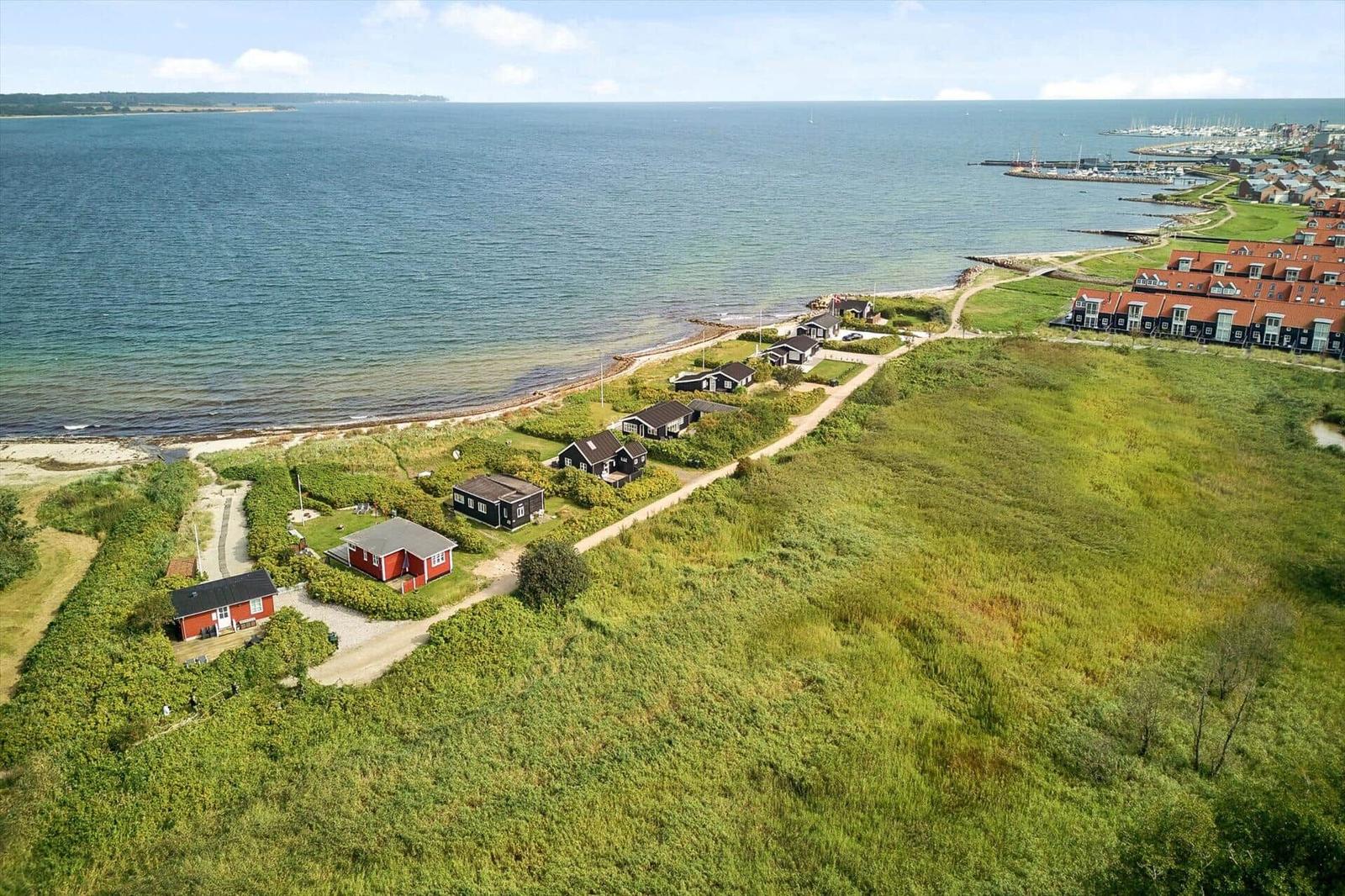 Küstenansicht mit roten und schwarzen Häusern, Grünflächen und Hafen im Hintergrund.