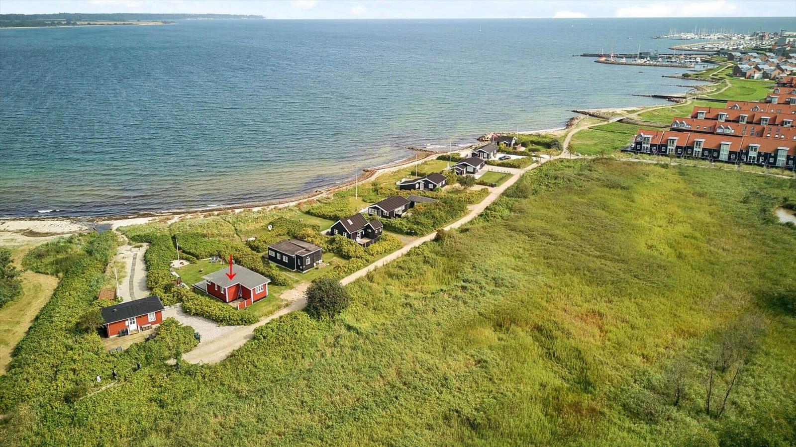 Rotes Strandhaus mit Garten, umgeben von Grünflächen und Meer.