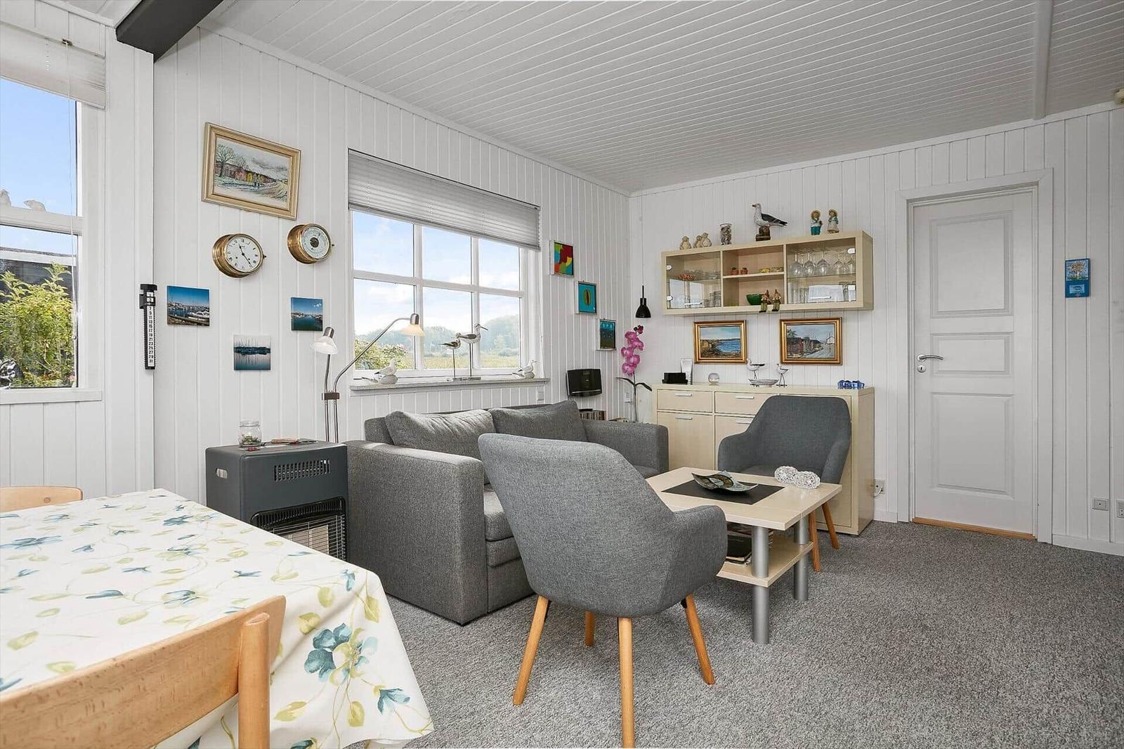 Wohn- und Essbereich mit grauem Sofa, Tisch und Stühlen. Weiße Wände und Fenster mit Blick.