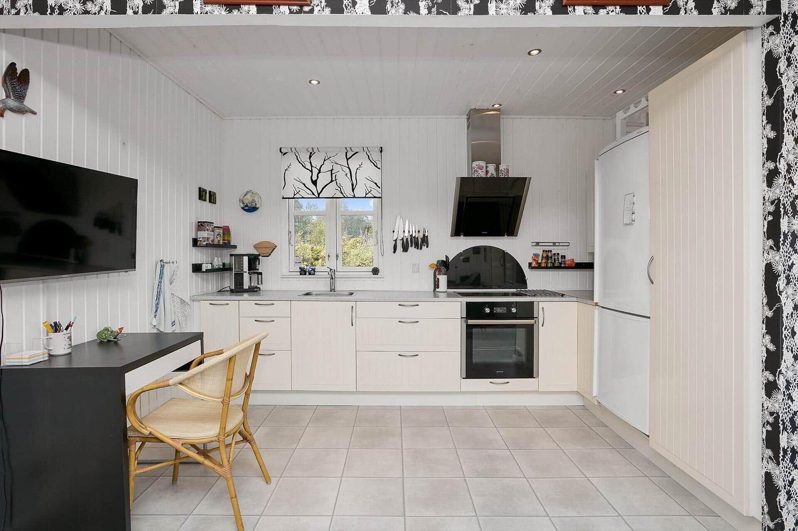 Küche mit weißer Einbauküche, Fenster, Kühlschrank und Arbeitsplatz.