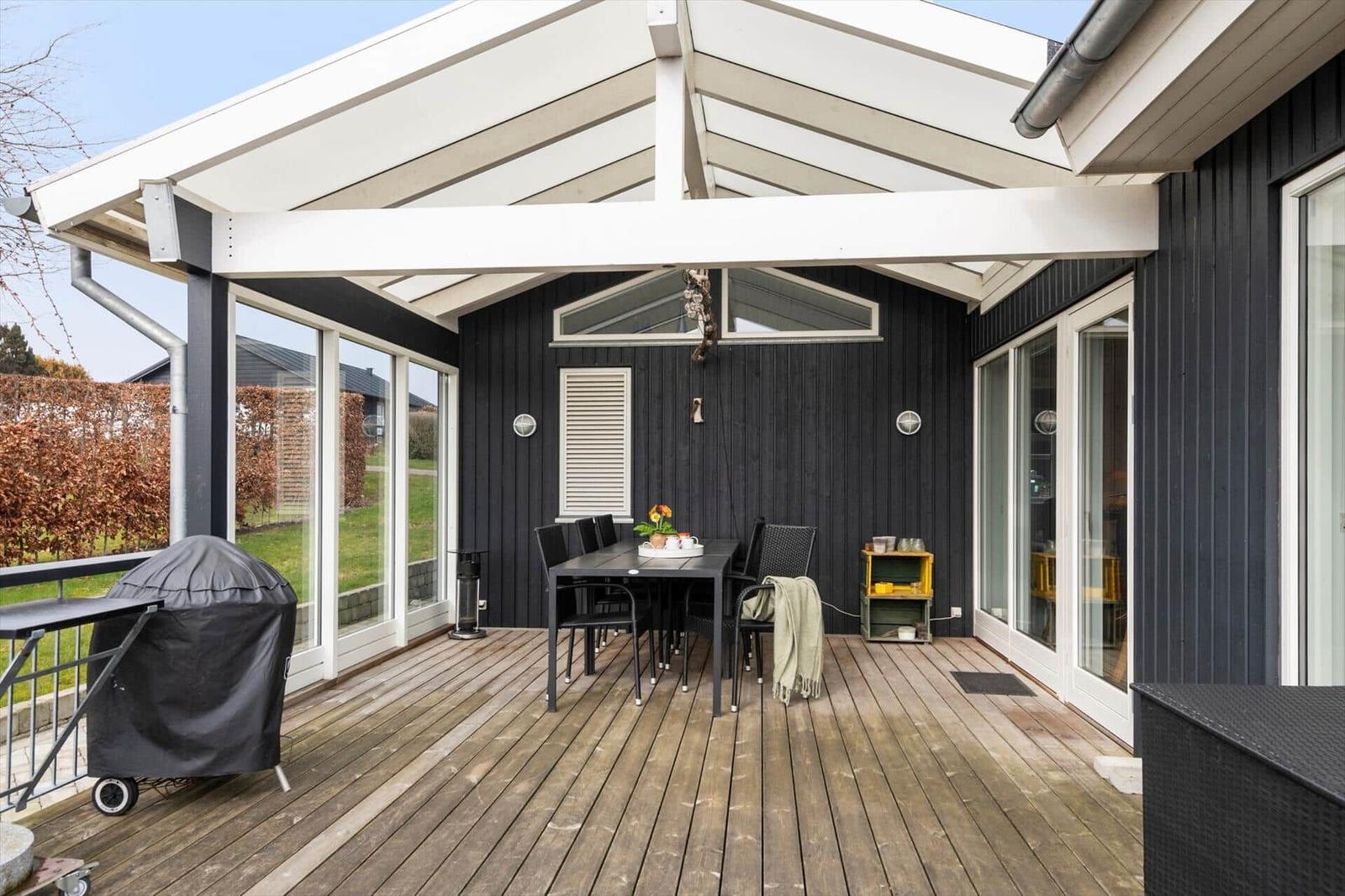 Terrasse mit Tisch, Stühlen und Grill unter weißem Dach