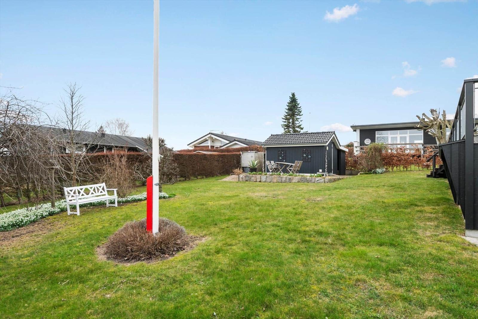 Grüner Garten mit weißer Bank, kleinem Haus und Bäumen im Hintergrund.