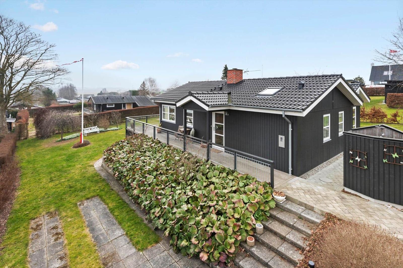 Schwarzes Haus mit Terrasse und Garten. Flagge weht im Wind.