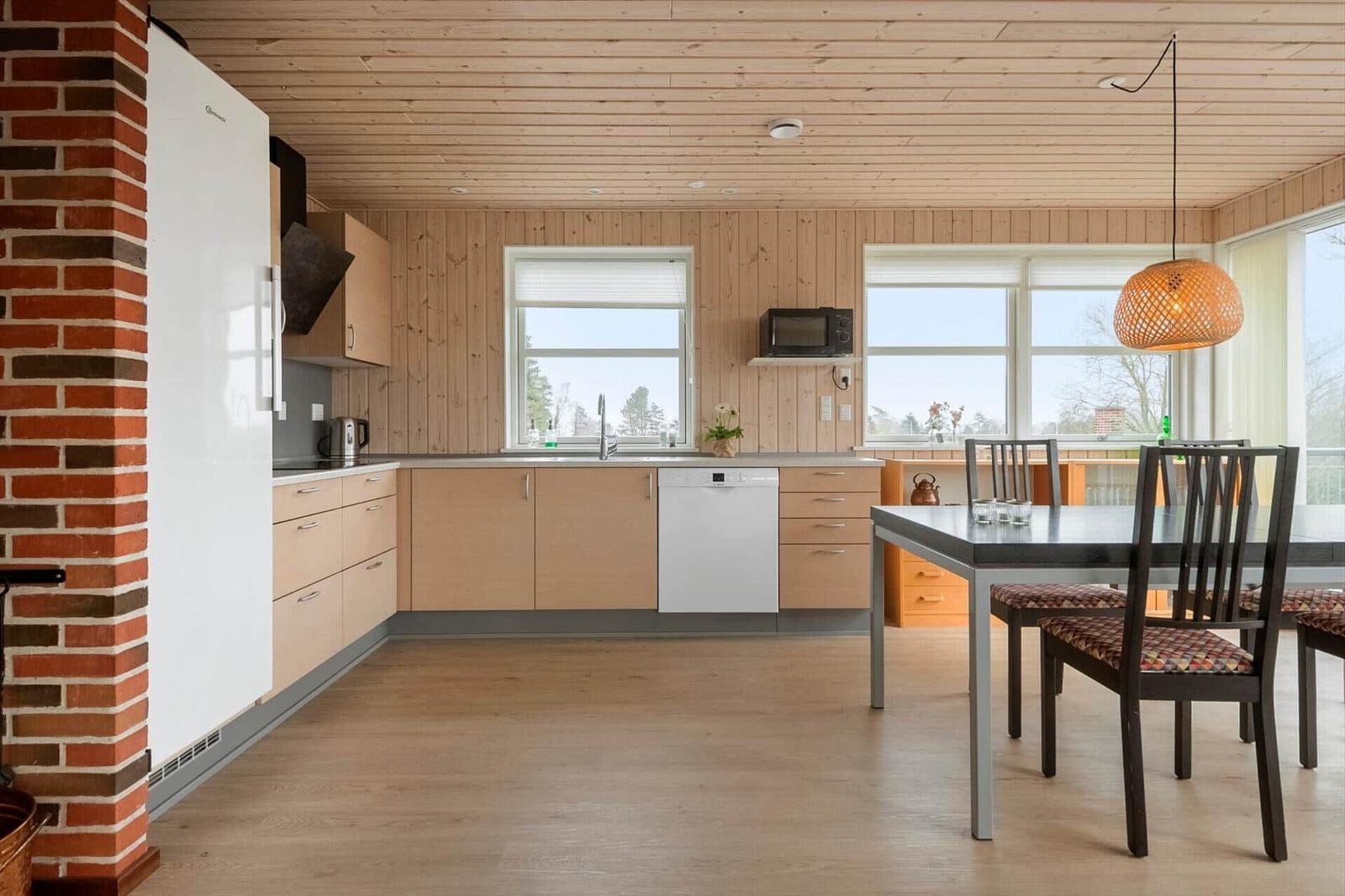 Küche mit Essbereich, Holzwand und Fenstern. Esstisch mit Stühlen und Deckenleuchte.