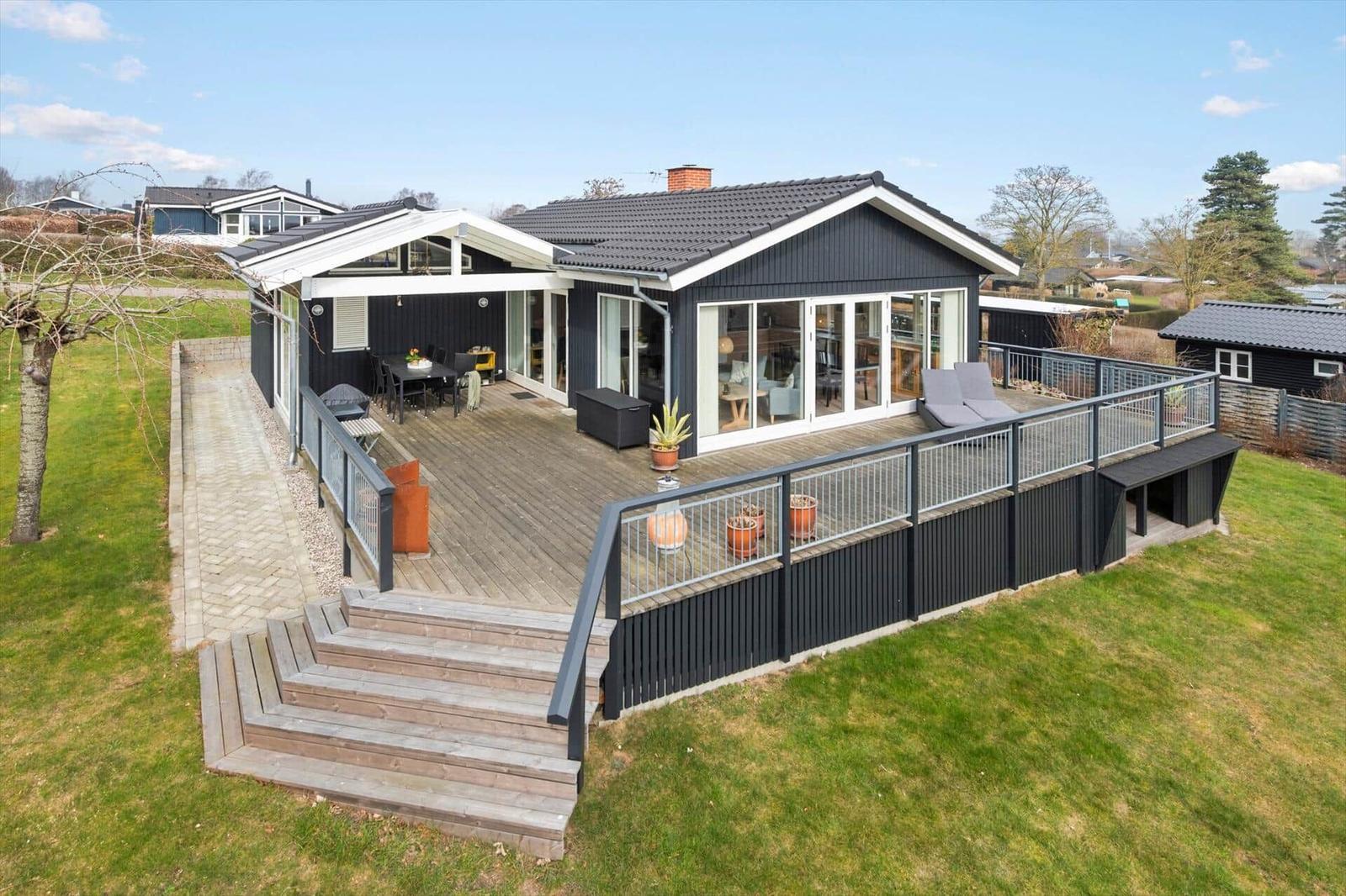Moderne Villa mit großem Holzterrasse, Garten und Terrassentür zur Küche.