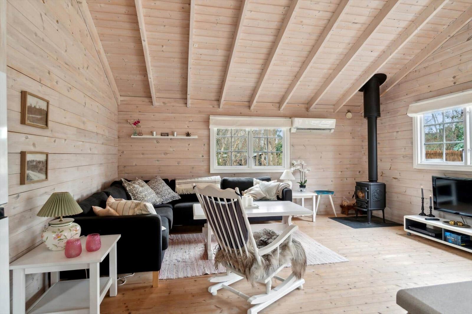 Wohnzimmer mit Holzwand, Sofa, Schaukelstuhl und Kaminofen.