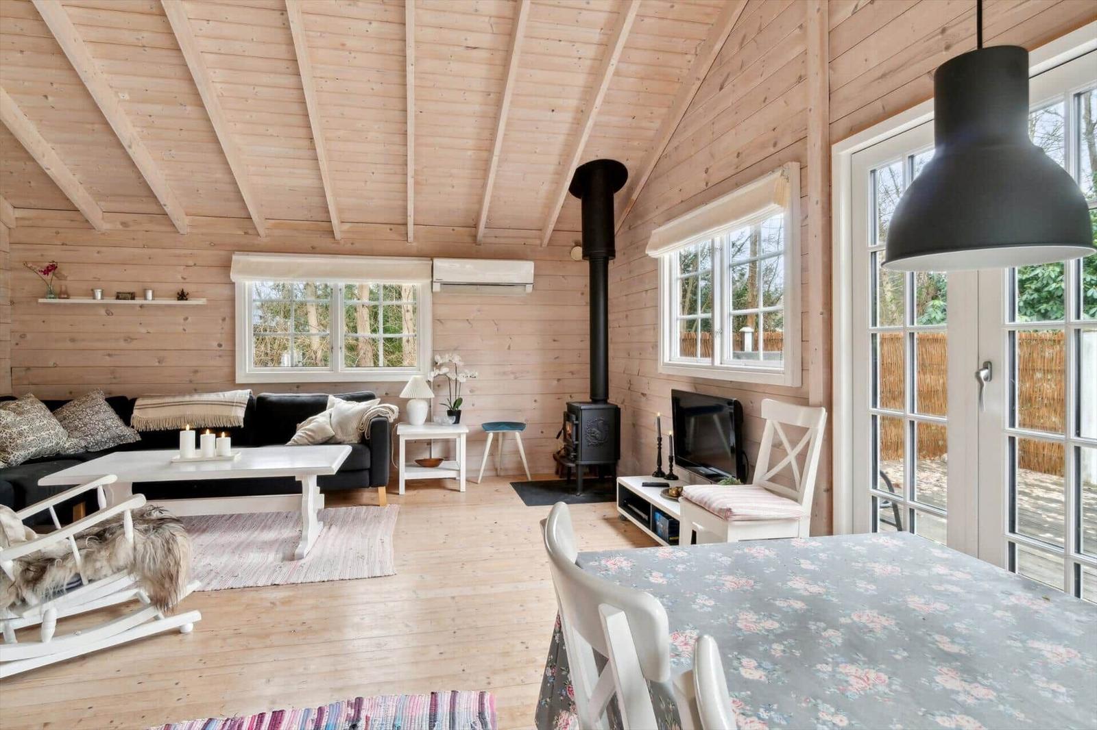 Wohnzimmer mit Holzwand, Kamin und Essbereich mit Tischdecke.