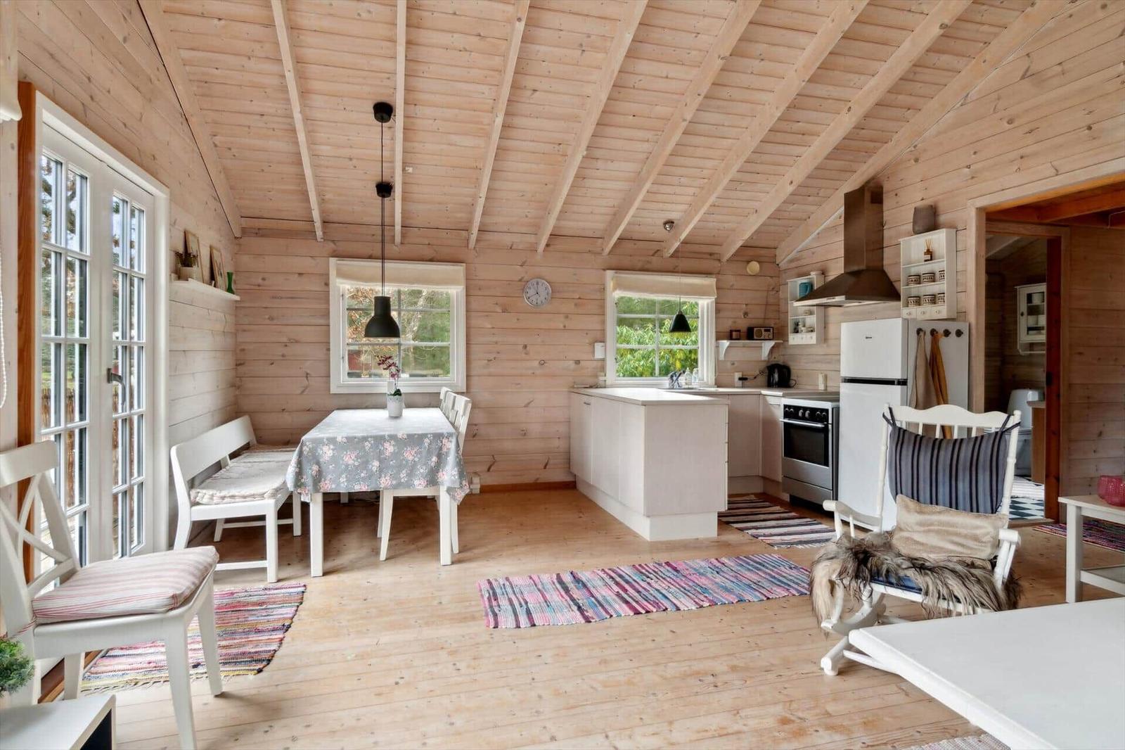 Holzhaus mit Küche, Esstisch und Sitzgelegenheiten. Weiße Möbel und Fenster.