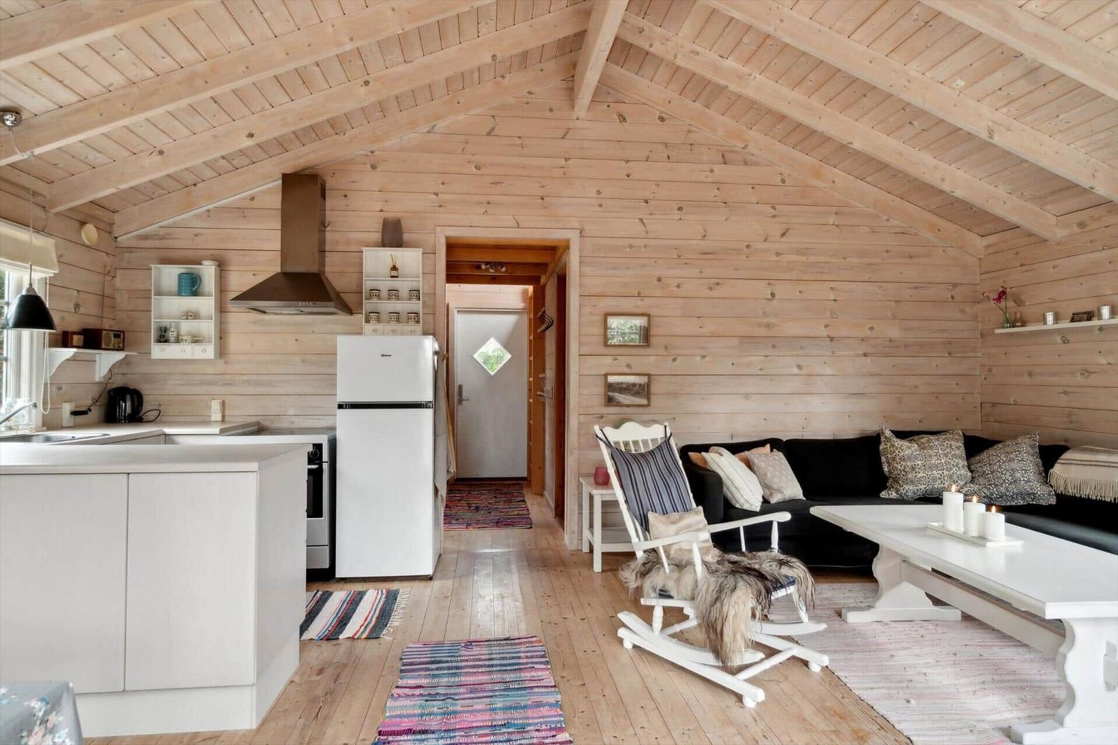 Wohnküche mit Holzwand und -decke, weißer Kühlschrank und Sitzgelegenheiten.