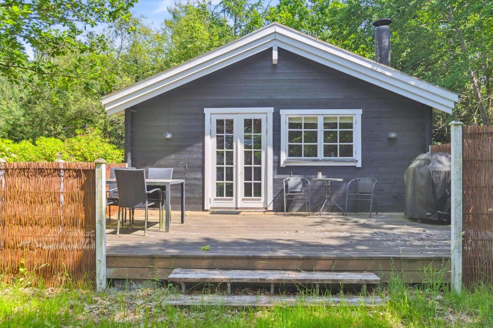 Ein dunkelgrauer Holzhaus mit weißem Dach und Terrasse mit Gartenmöbeln.