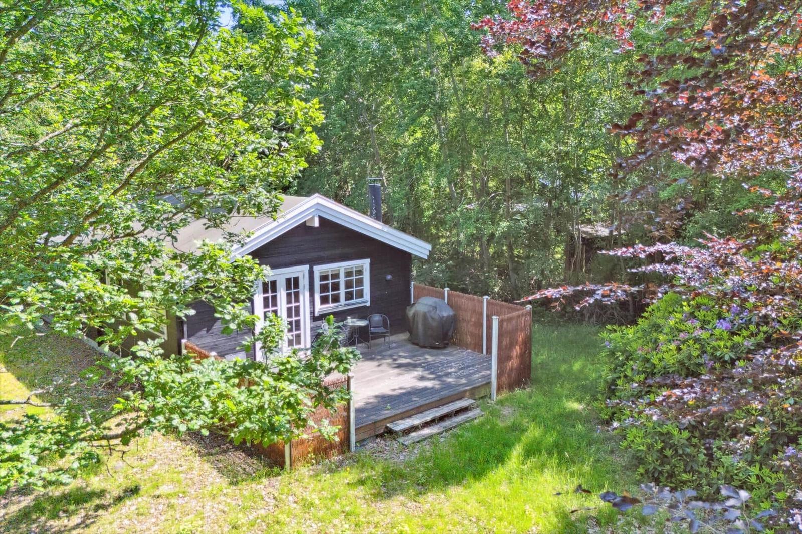Holzhaus mit Terrasse im Grünen, umgeben von Bäumen und Sträuchern.