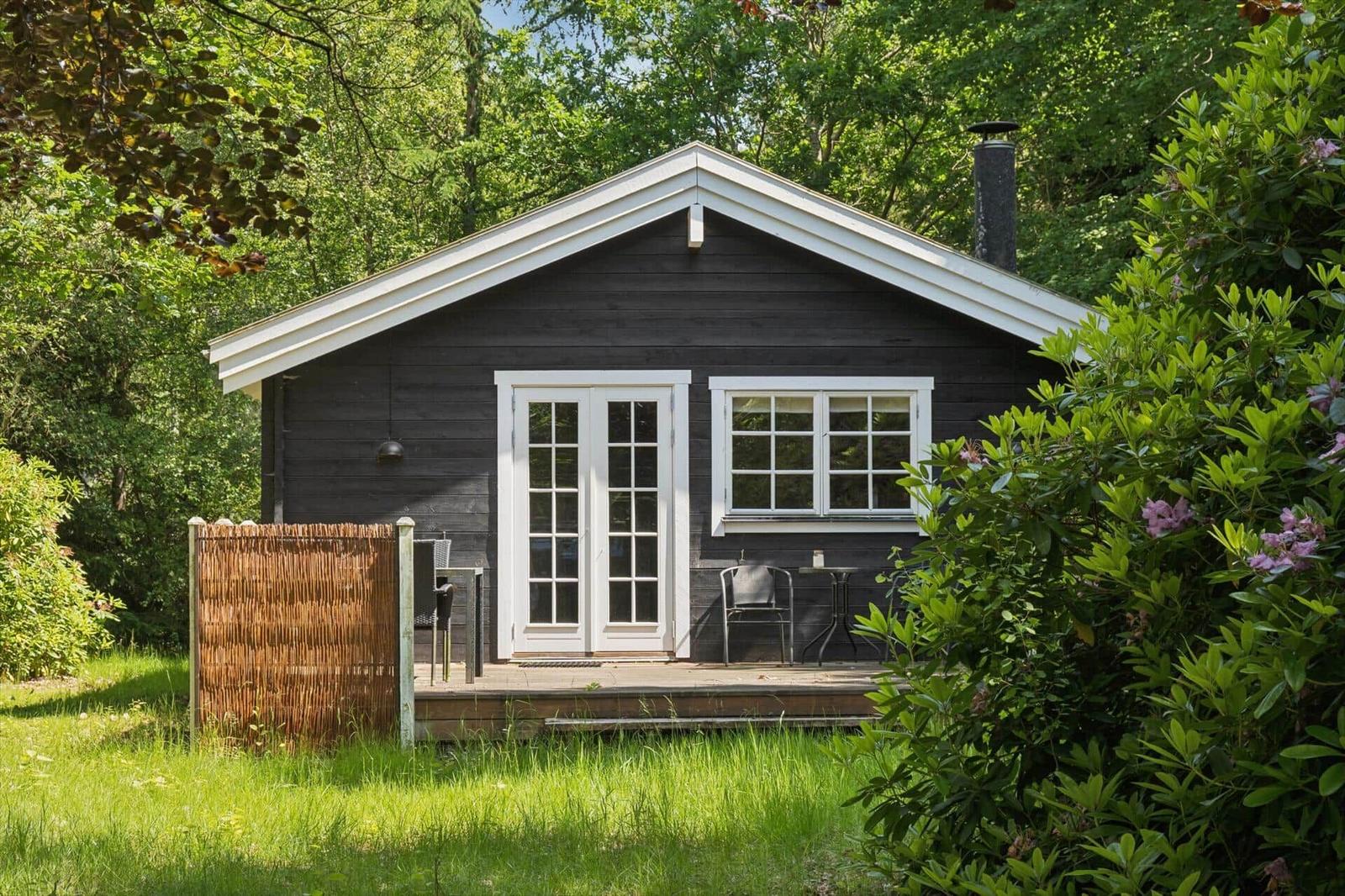 Schwarzes Holzhaus mit weißen Fenstern und Terrasse im Grünen.