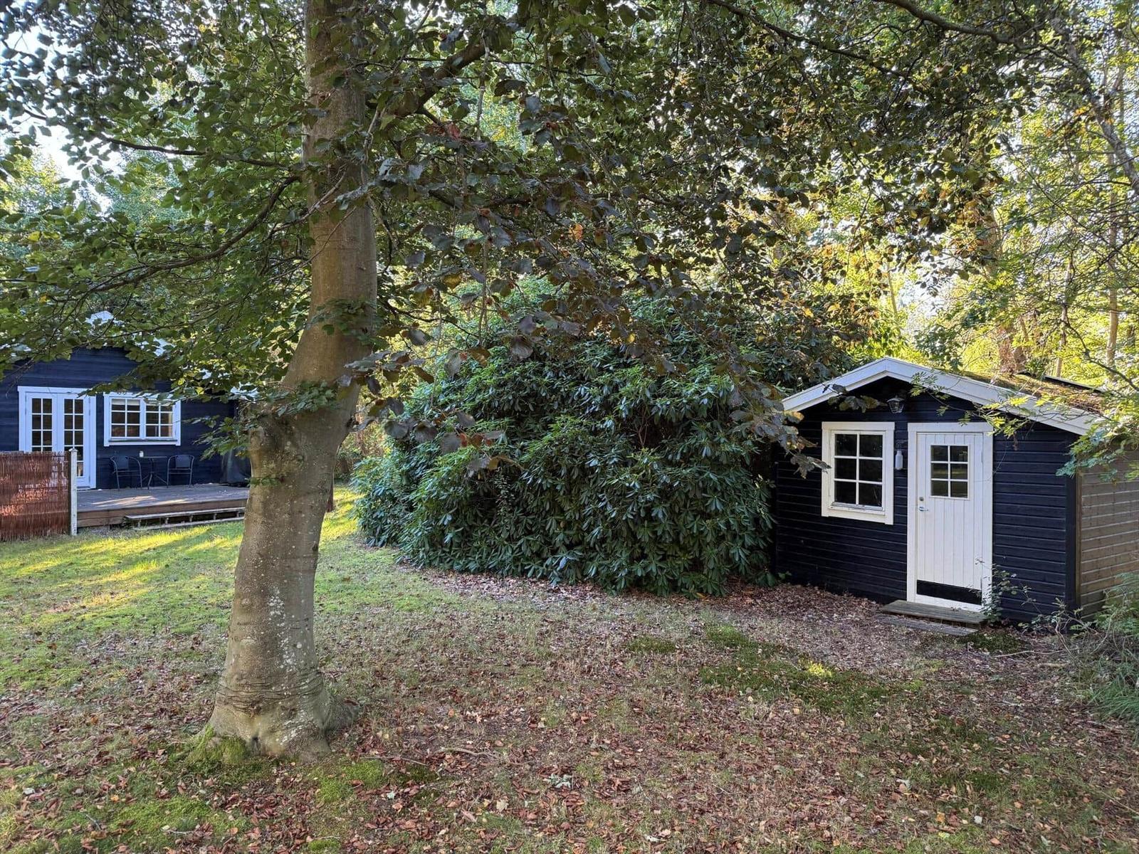Zwei schwarze Hütten mit weißen Fenstern und Türen im Wald. Gras und Bäume umgeben die Gebäude.