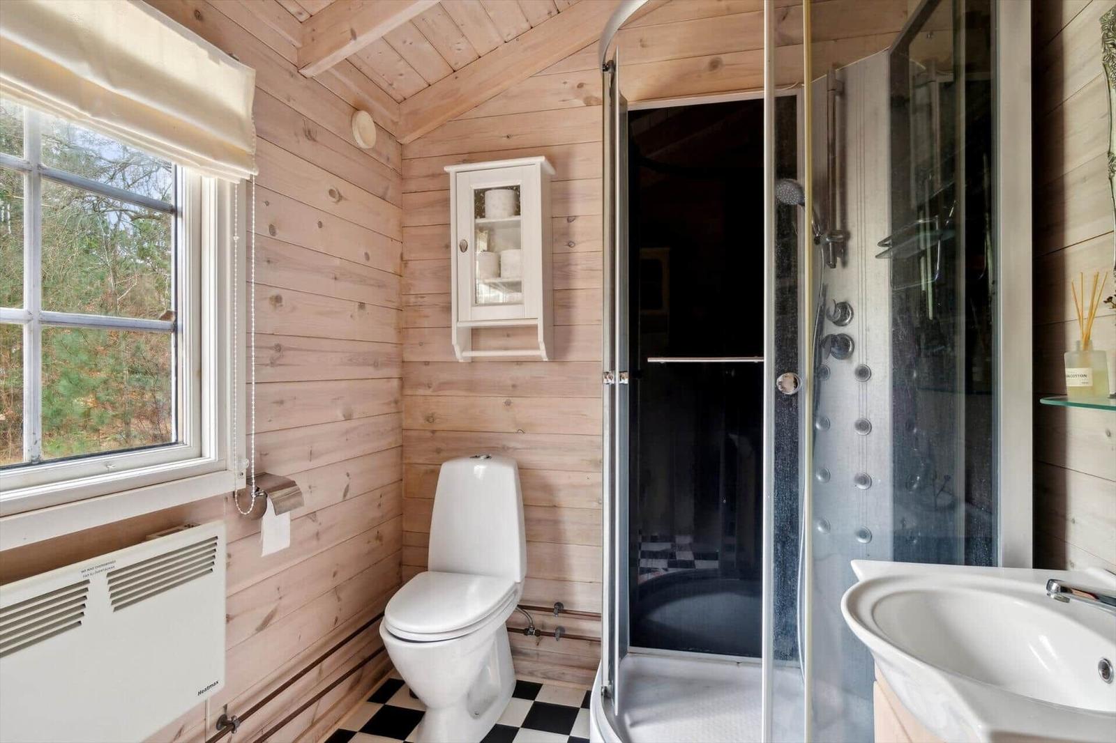 Badezimmer mit Dusche, Toilette und Waschbecken. Holzwände und schwarz-weißes Fliesenboden.