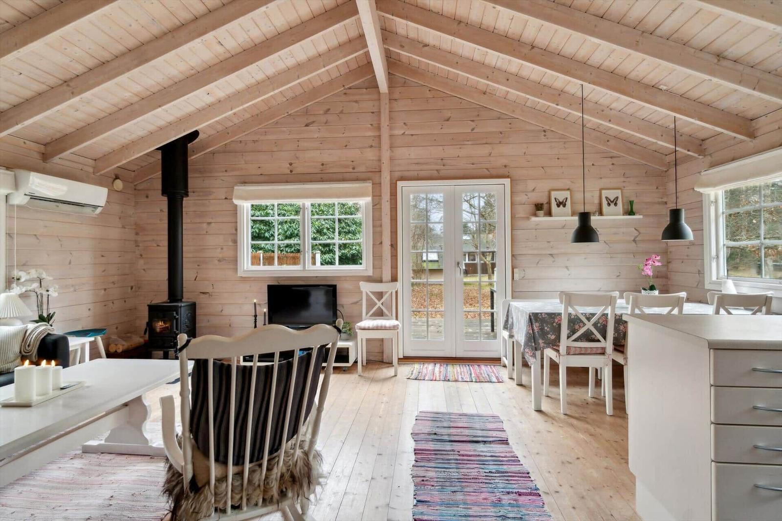 Wohnraum mit Holzdecke, Kamin und Essbereich mit Tisch und Stühlen.