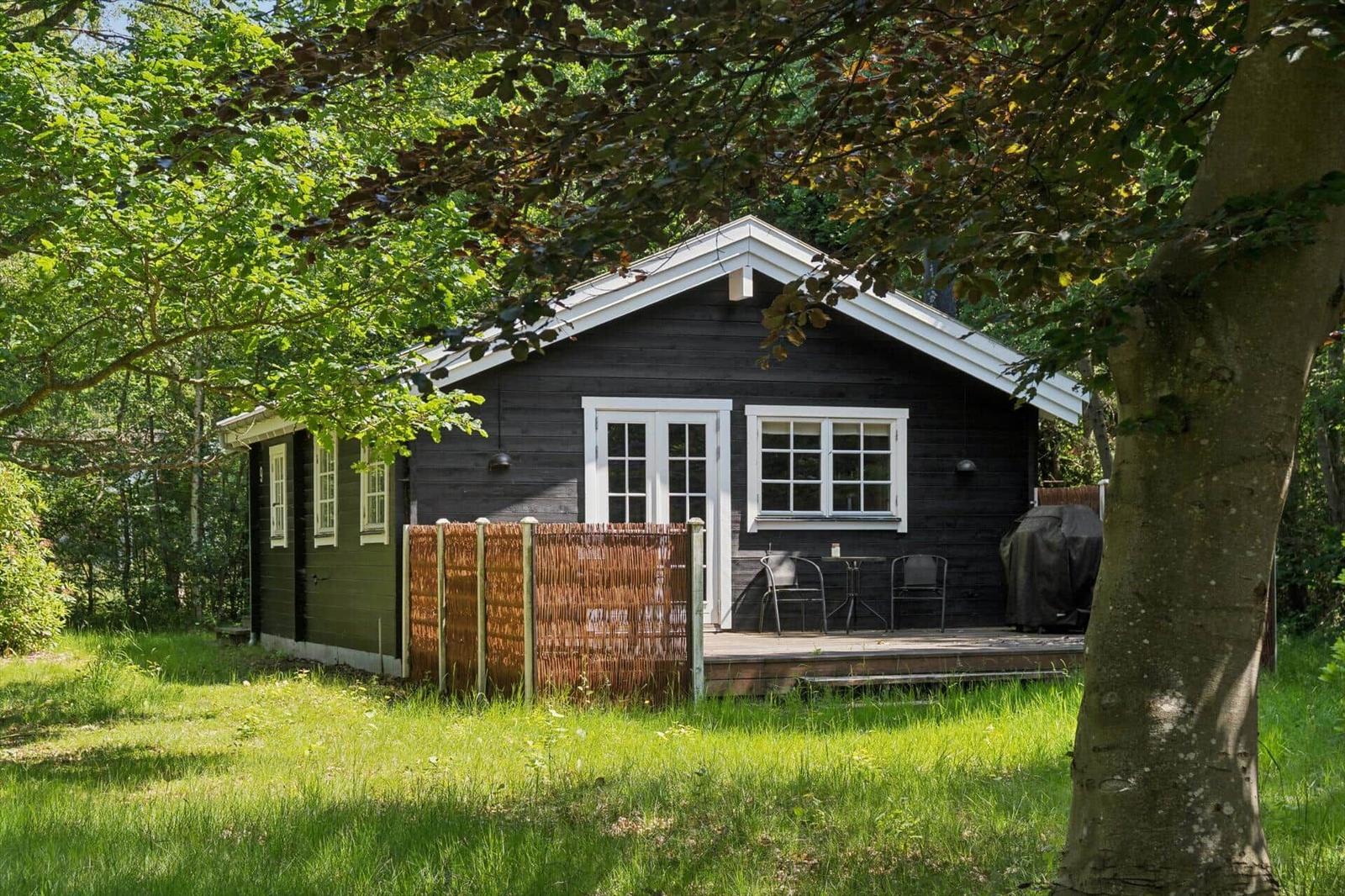Holzhütte mit Terrasse, umgeben von Bäumen und Gras.