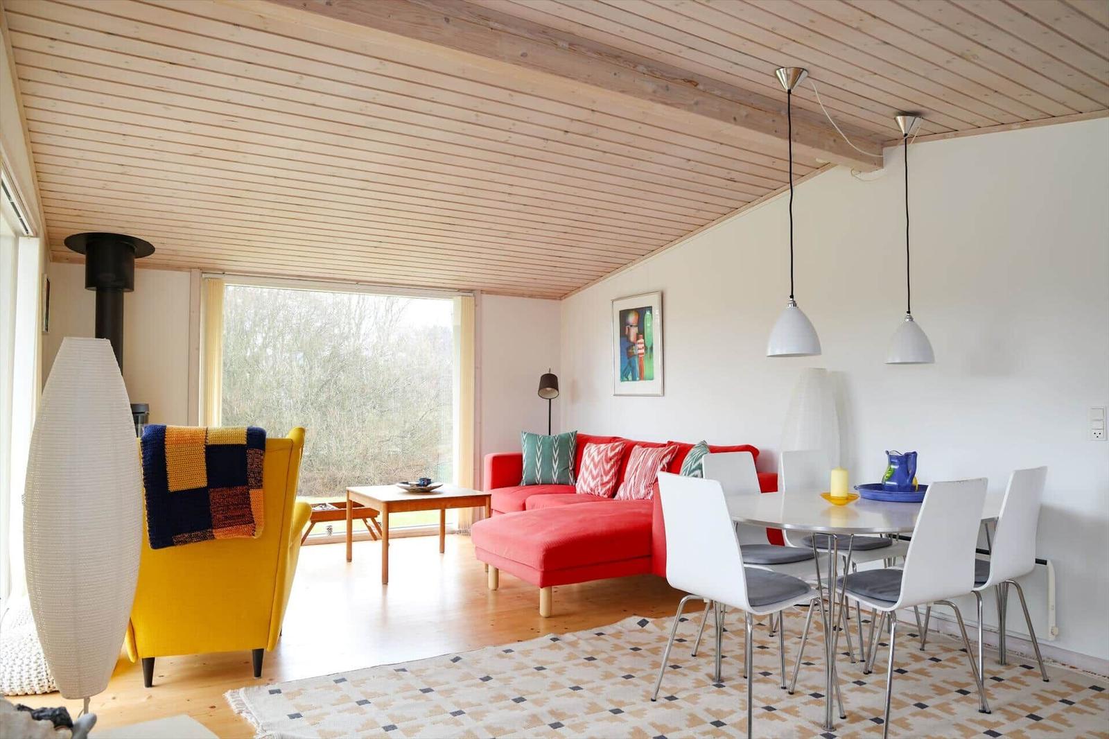 Wohn- und Essbereich mit rotem Sofa, gelber Sitzgelegenheit und Esstisch mit Stühlen.