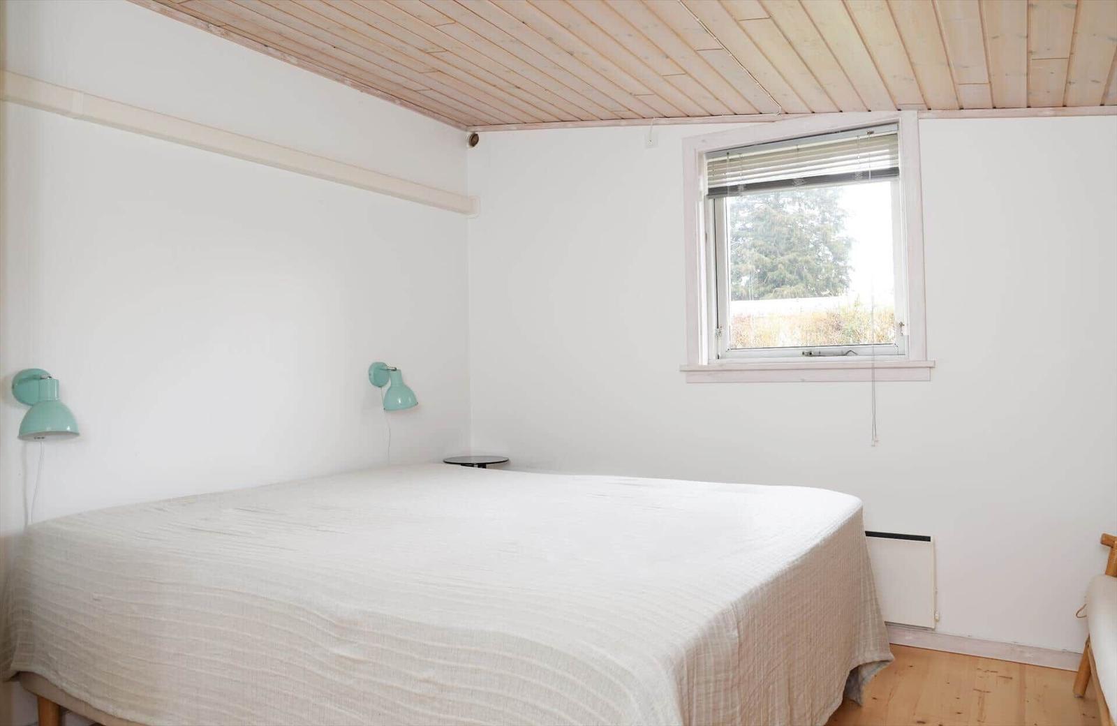Schlafzimmer mit Bett, Fenster und Holzdecke.