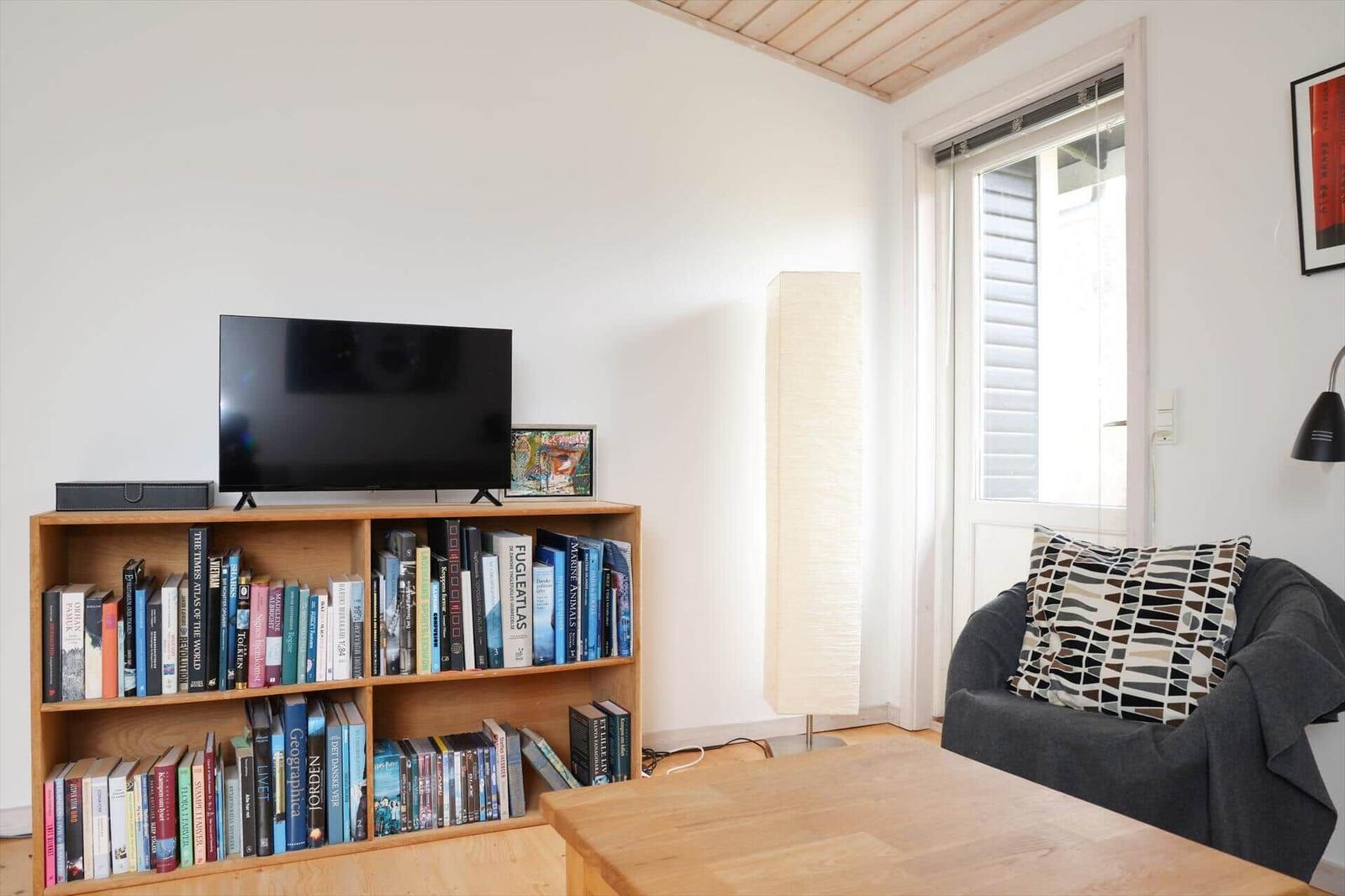 Wohnzimmer mit Fernseher, Bücherregal und Sessel.