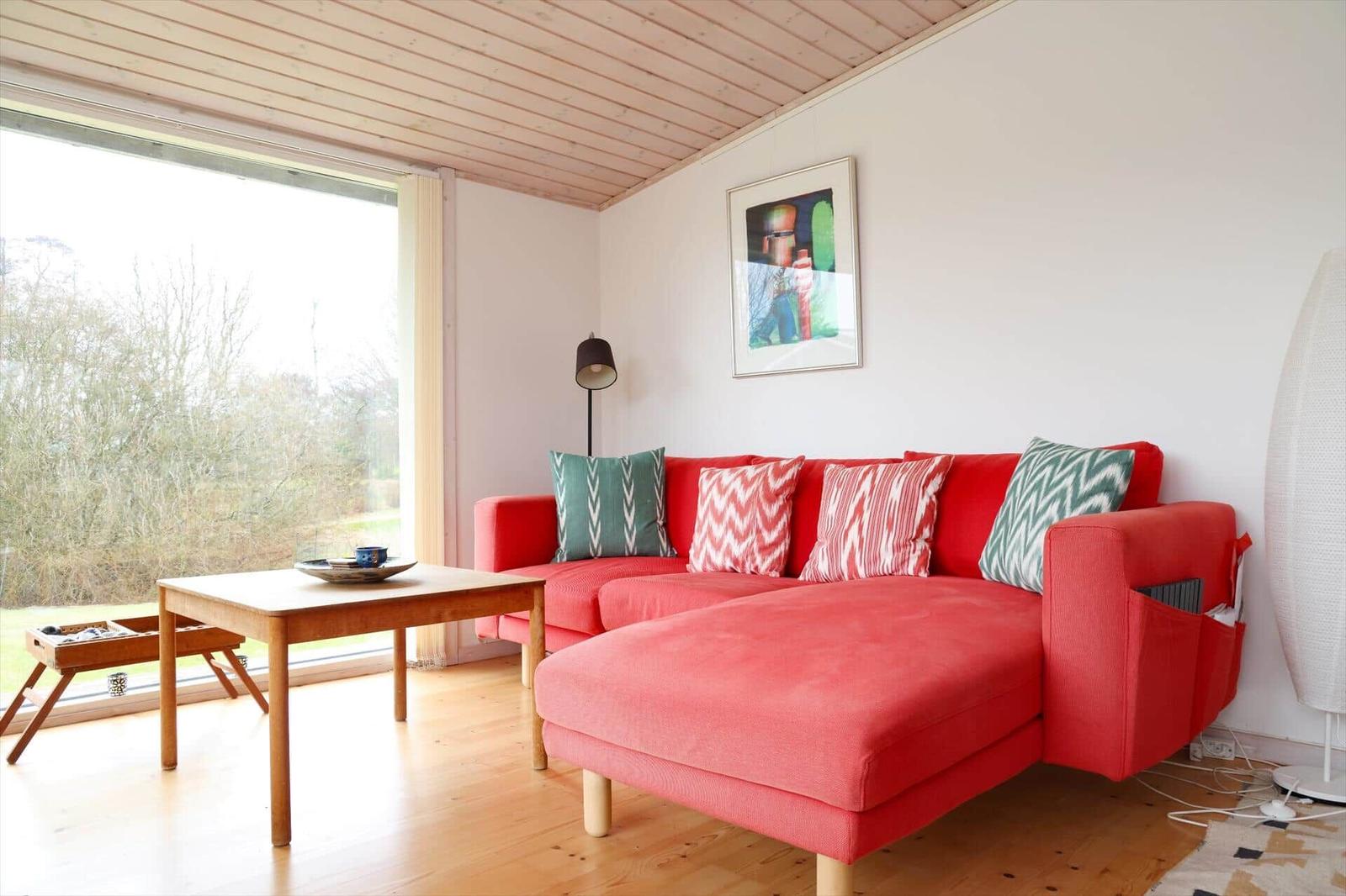 Ein Wohnzimmer mit rotem Sofa, Holzboden und großem Fenster zur Außenseite.