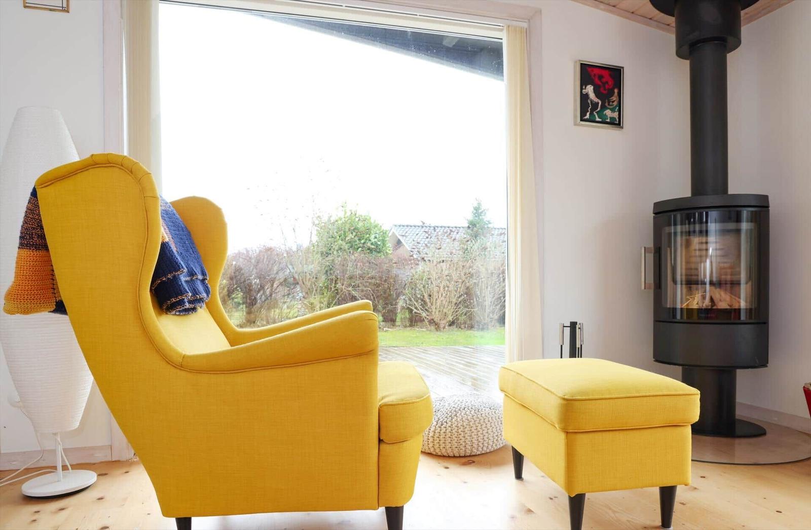 Gelber Sessel und Hocker neben Kamin und Fenster mit Blick auf Garten.