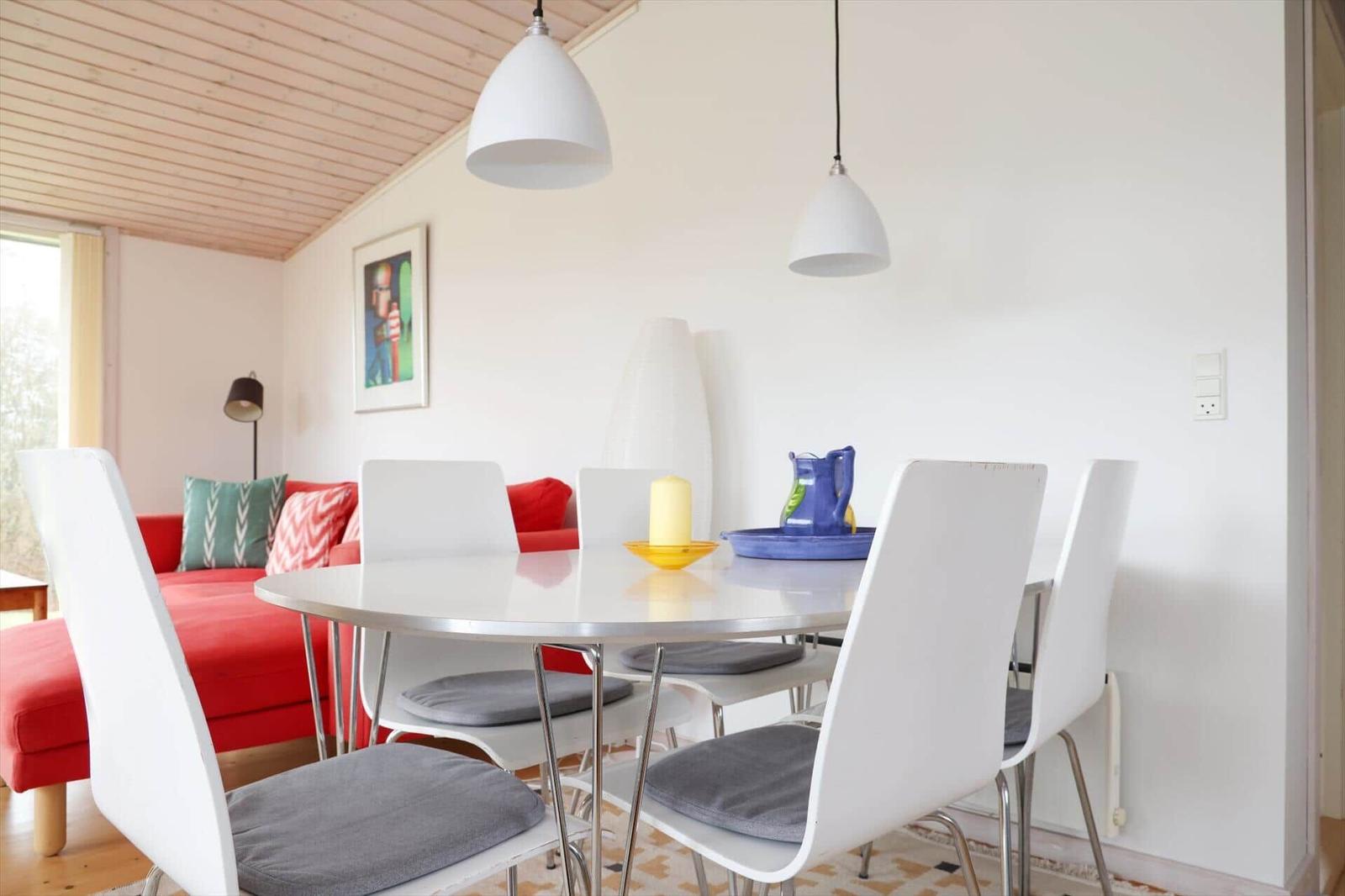 Essbereich mit runder Tisch und weißen Stühlen. Roter Sofa im Hintergrund.
