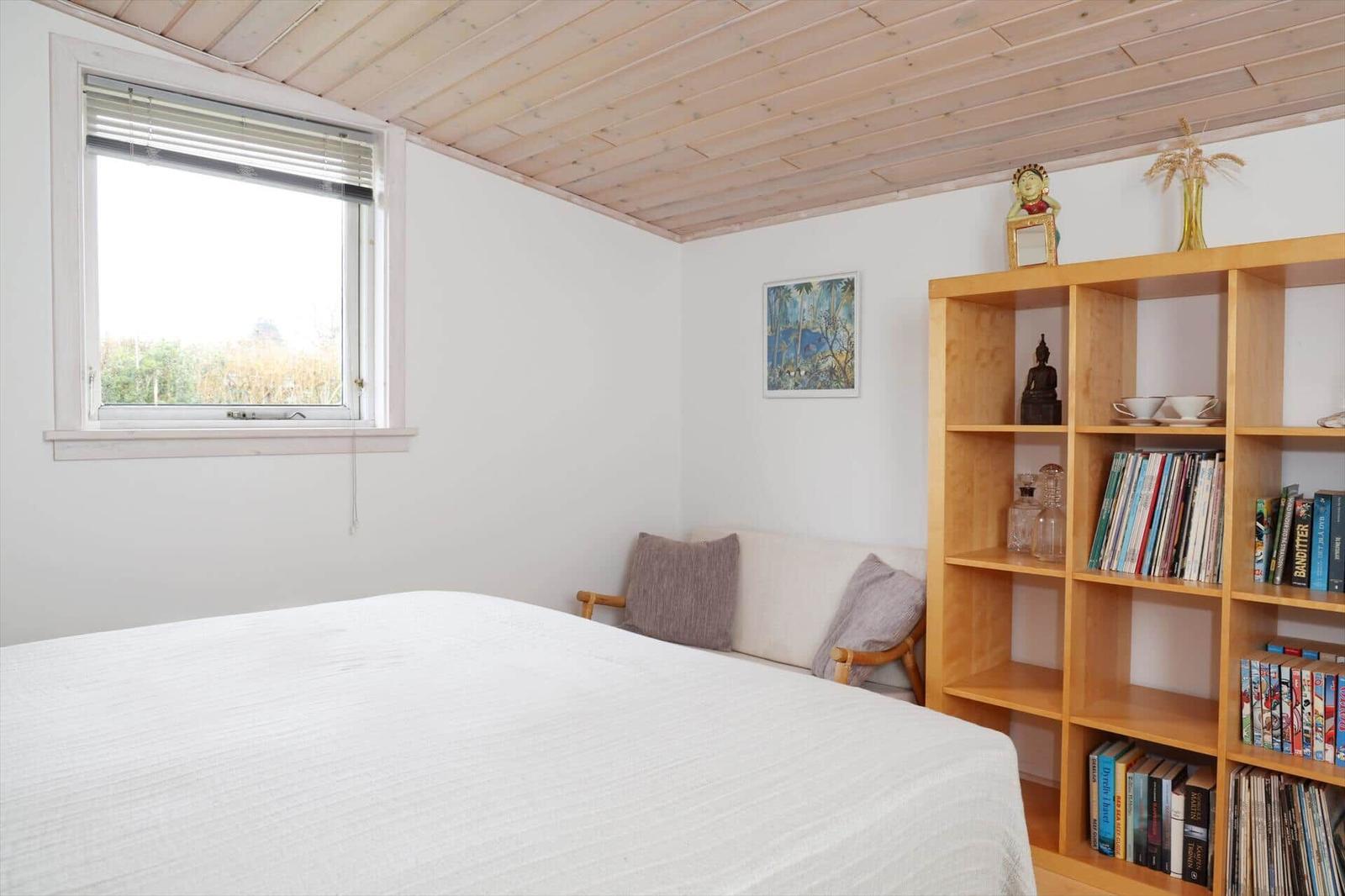 Schlafzimmer mit Bett, Fenster, Bücherregal und Wandbild.