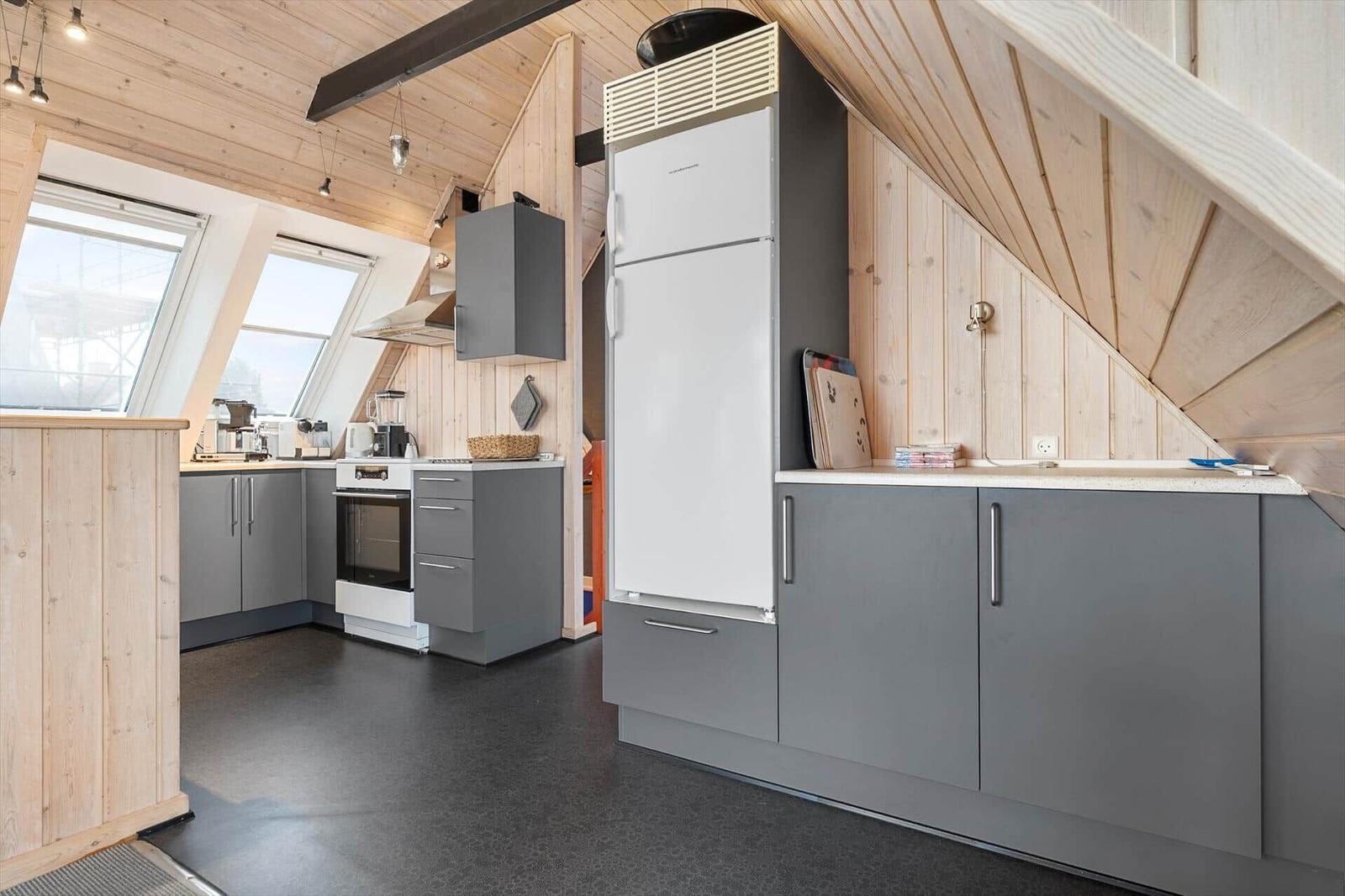 Küche mit grauen Schränken, weißem Kühlschrank und Holzwänden unter Dachschrägen.