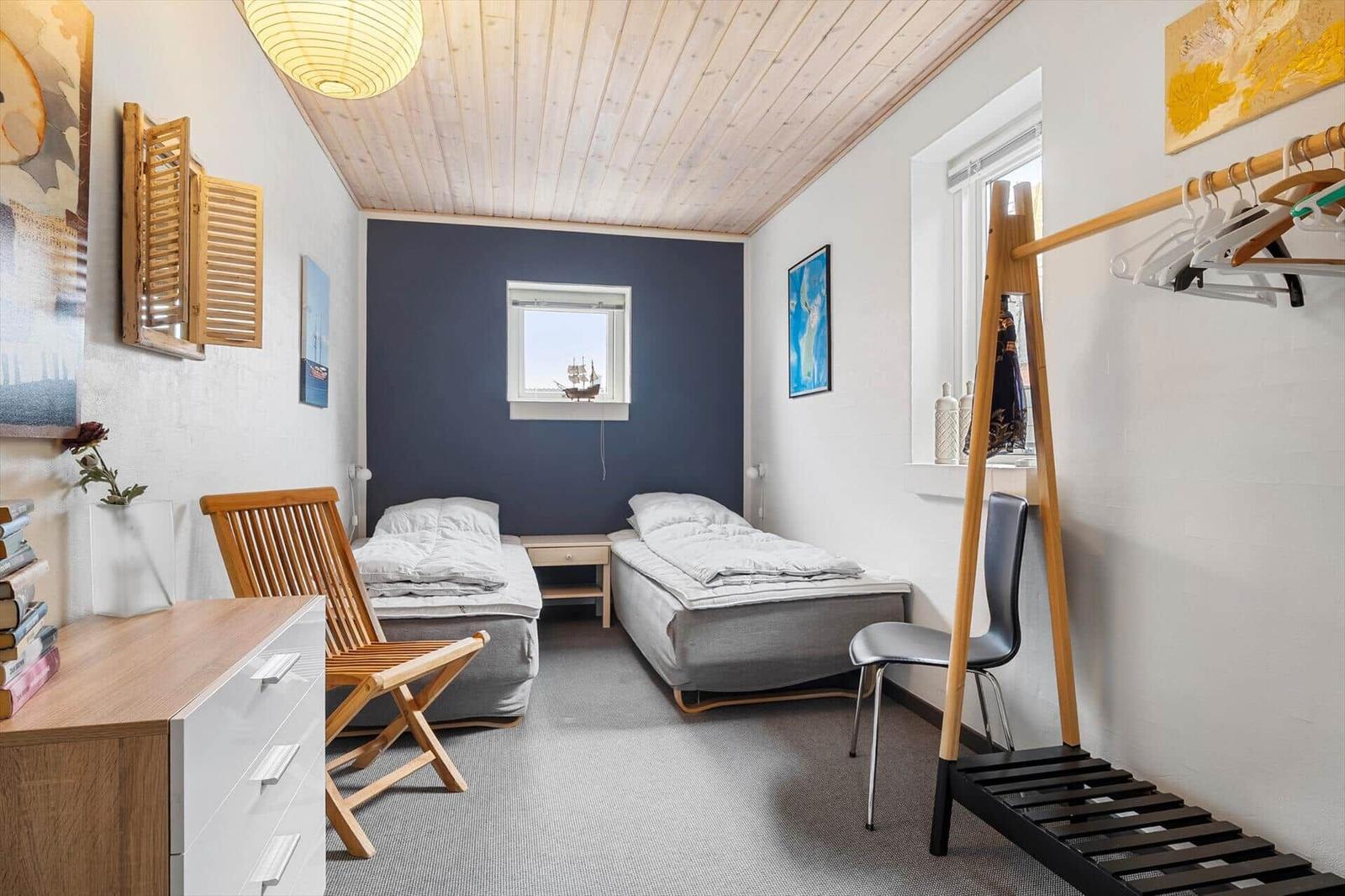 Zwei Betten, Kleiderständer und Fenster in einem Schlafzimmer mit Holzdecke.