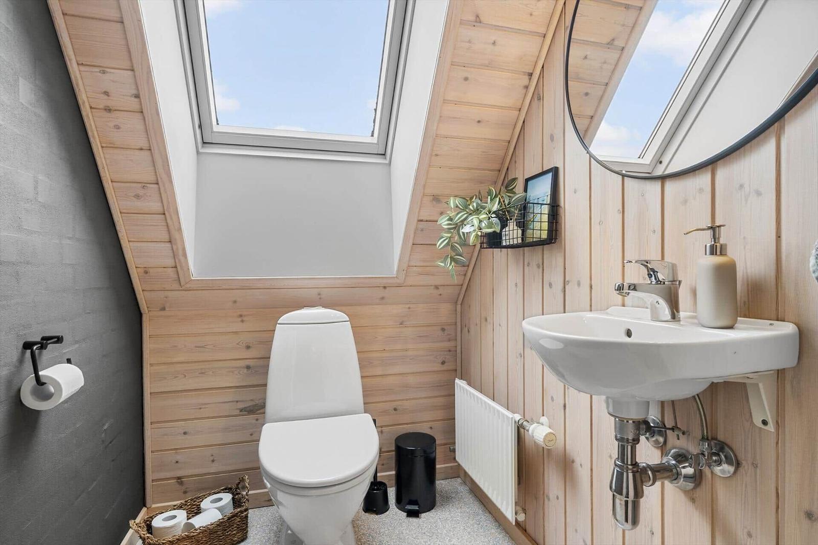 Badezimmer mit Toilette, Waschbecken und Dachfenster. Holzwände und graue Wand.