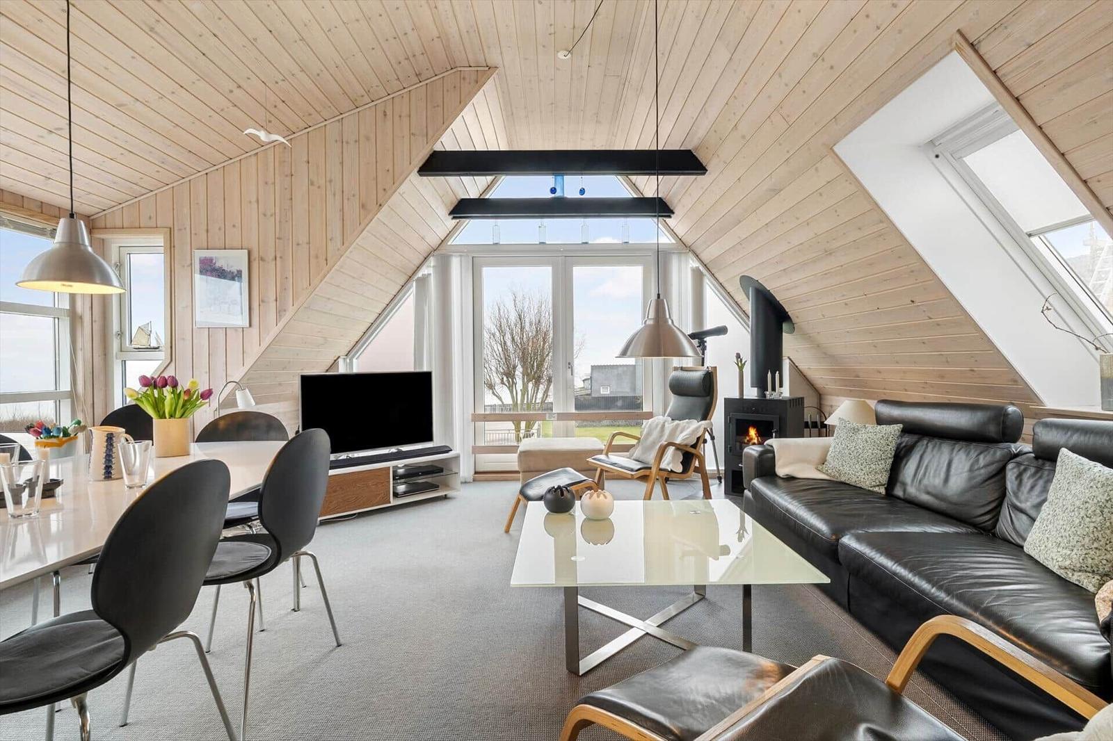 Wohn- und Essbereich mit Holzdecke, Sofa, TV und Fenstern.