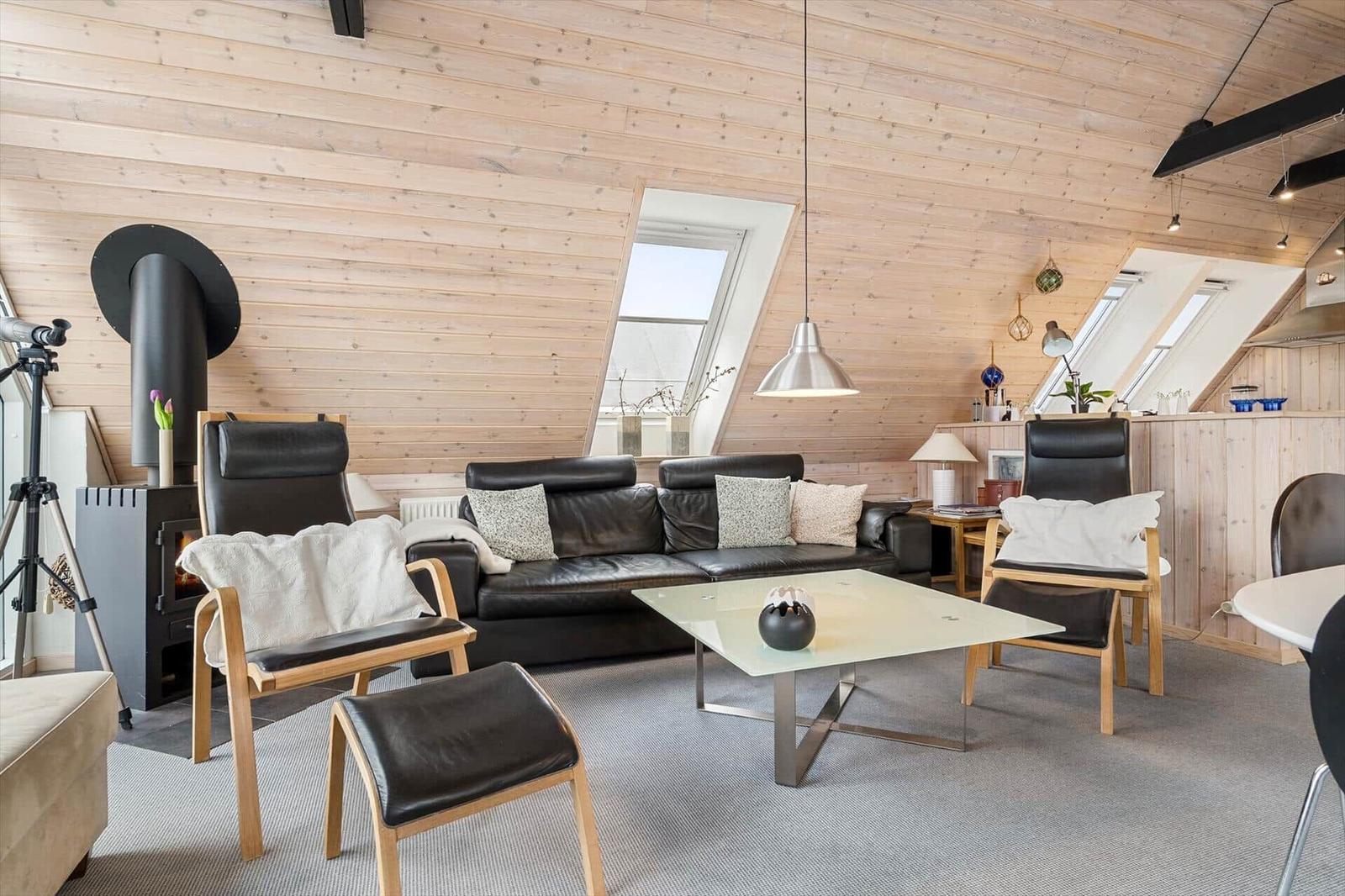 Wohnraum mit Holzwand, Sofa, Stühlen und Kamin.