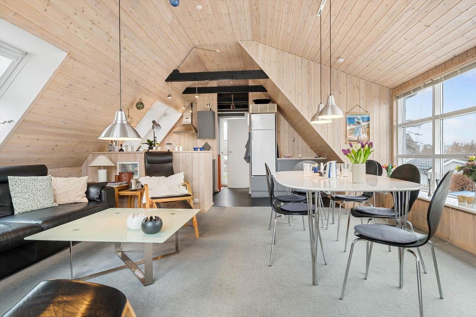 Wohnbereich mit Essbereich, Holzdecke und Fenster. Sofa, Tisch und Stühle sichtbar.