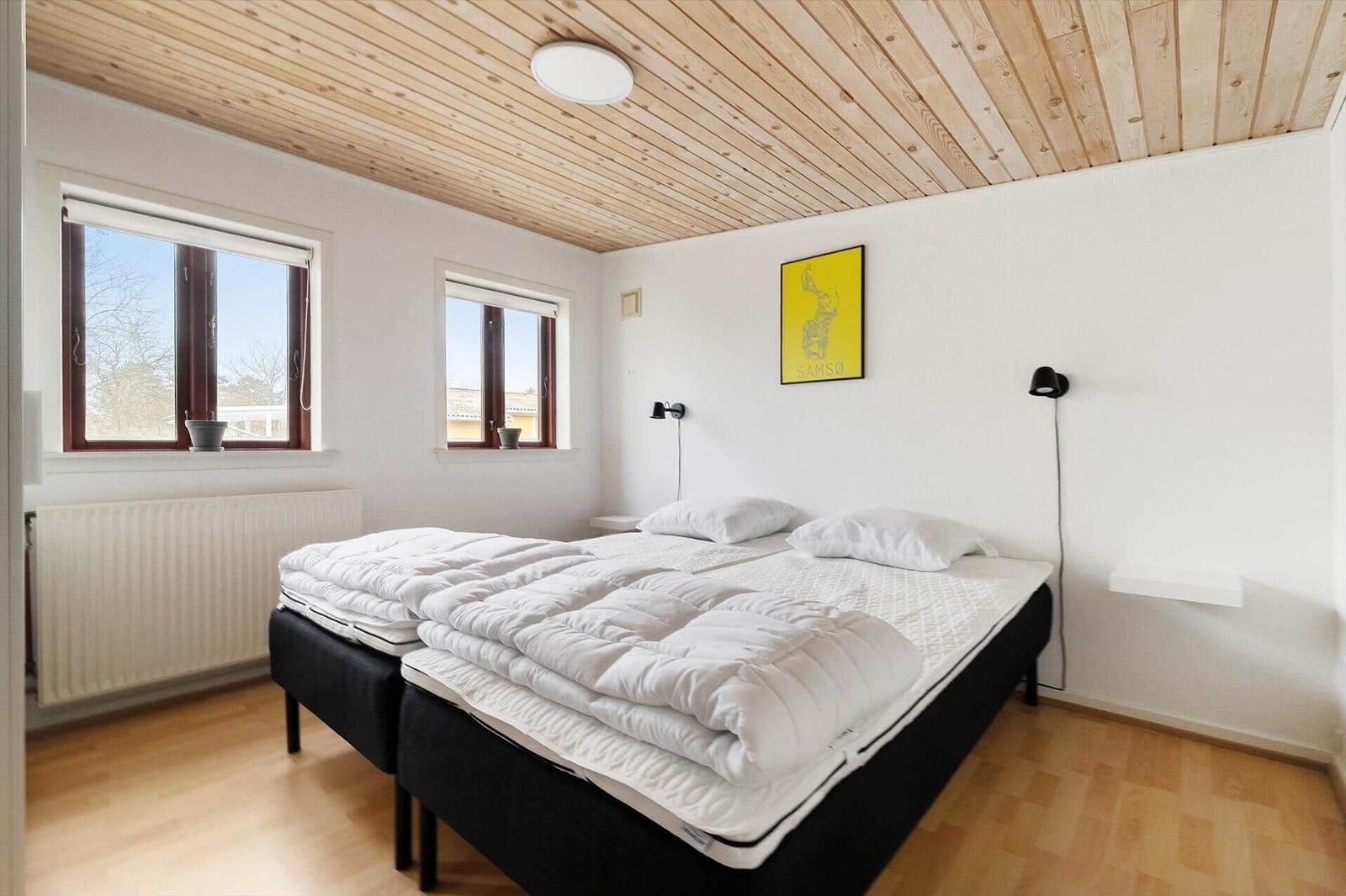 Schlafzimmer mit Doppelbett, Holzdecke und zwei Fenstern.