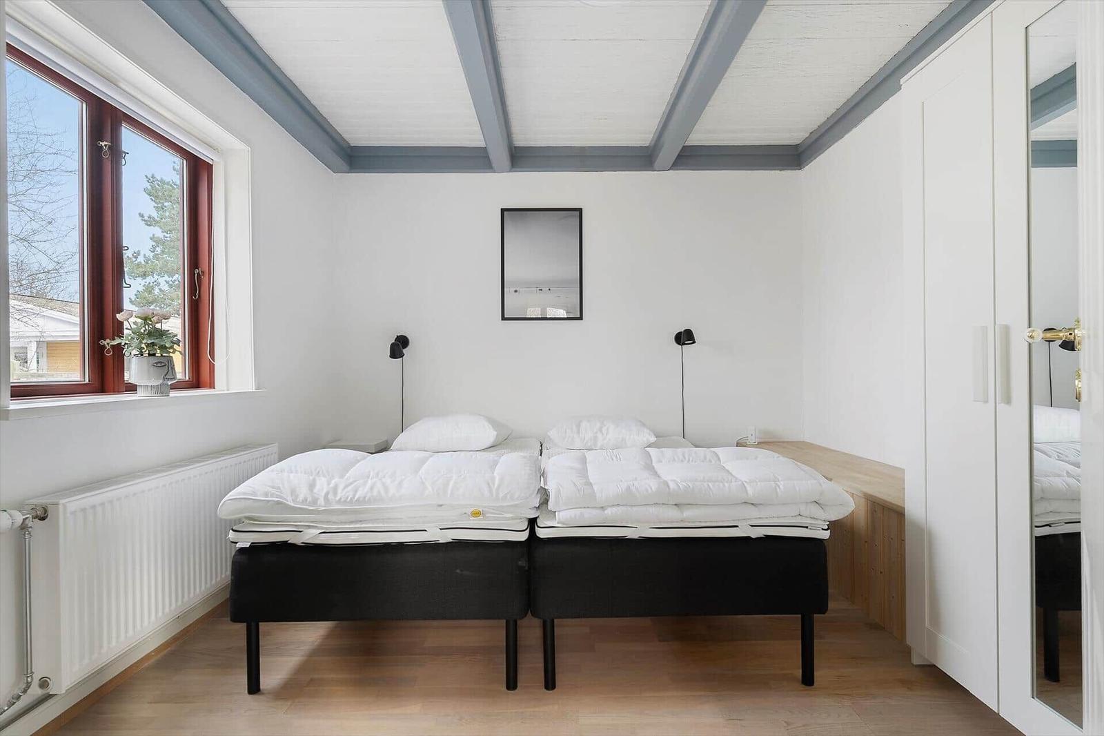Zwei Schlafplätze mit Matratzen und weißen Bettwäschen. Fenster mit rotem Rahmen und Spiegel an der Wand.